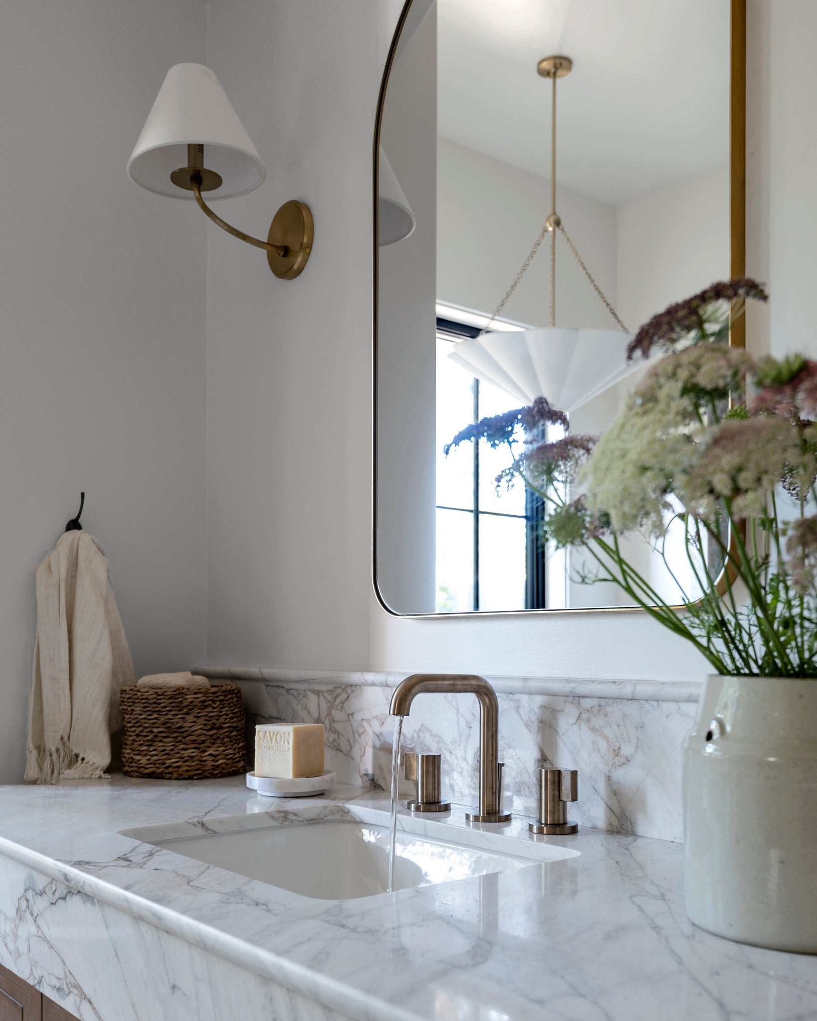 Stacey Wall Sconce in aged brass styled in a modern bathroom for warm, layered light at Laurie Yapp Home.