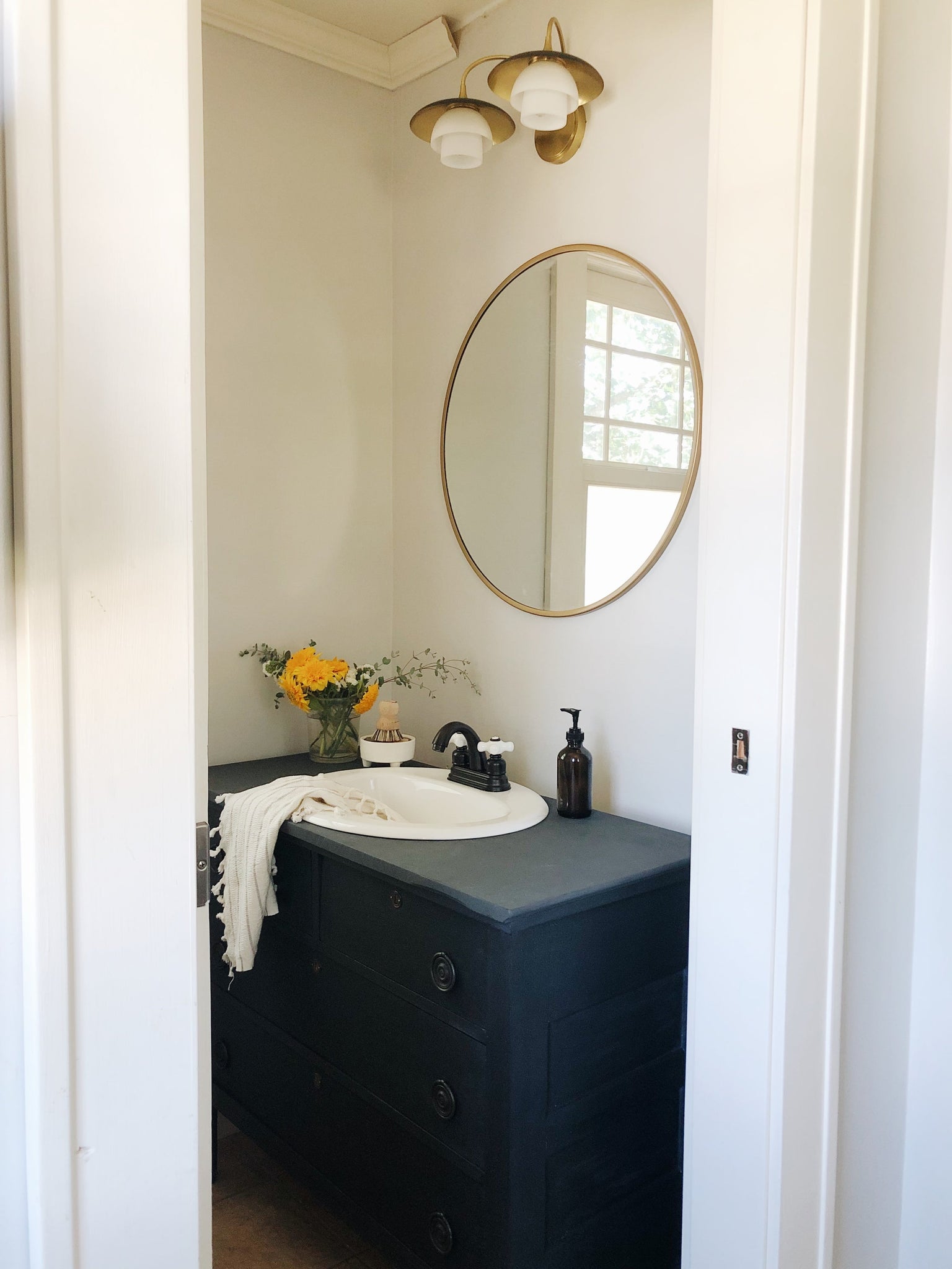 Barron Bath & Vanity in aged brass styled in a bright bathroom for warm, layered light at Laurie Yapp Home.
