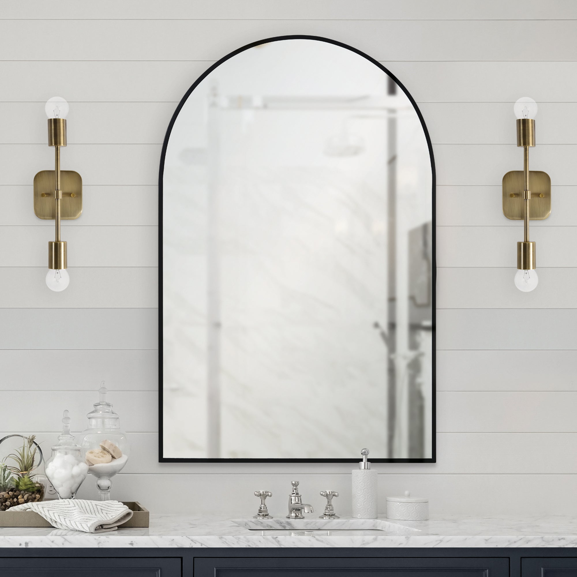 Waren Wall Mirror mounted above a sink, flanked by brass sconces in a bathroom setting.
