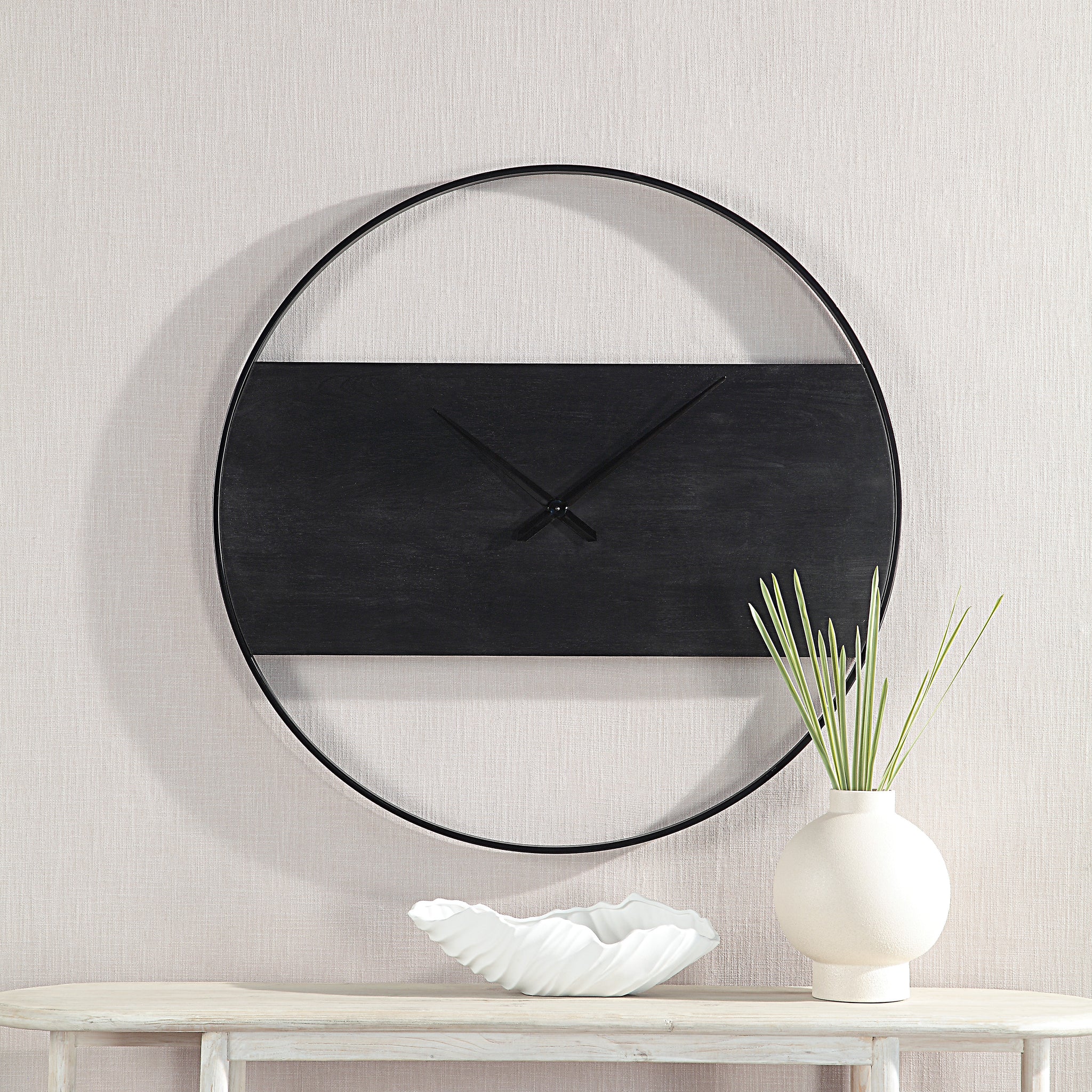 Romy Wall Clock mounted on a wall with decorative vase and bowl below