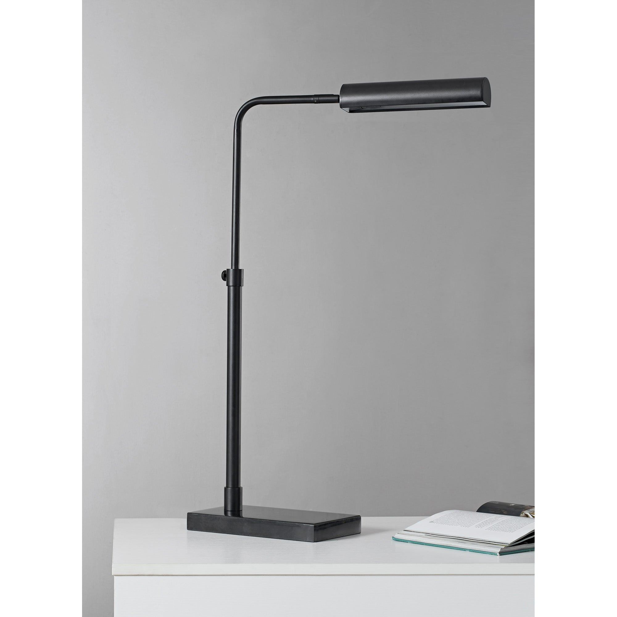 Fabolia Table Lamp in black, positioned on a desk with a book beside it.