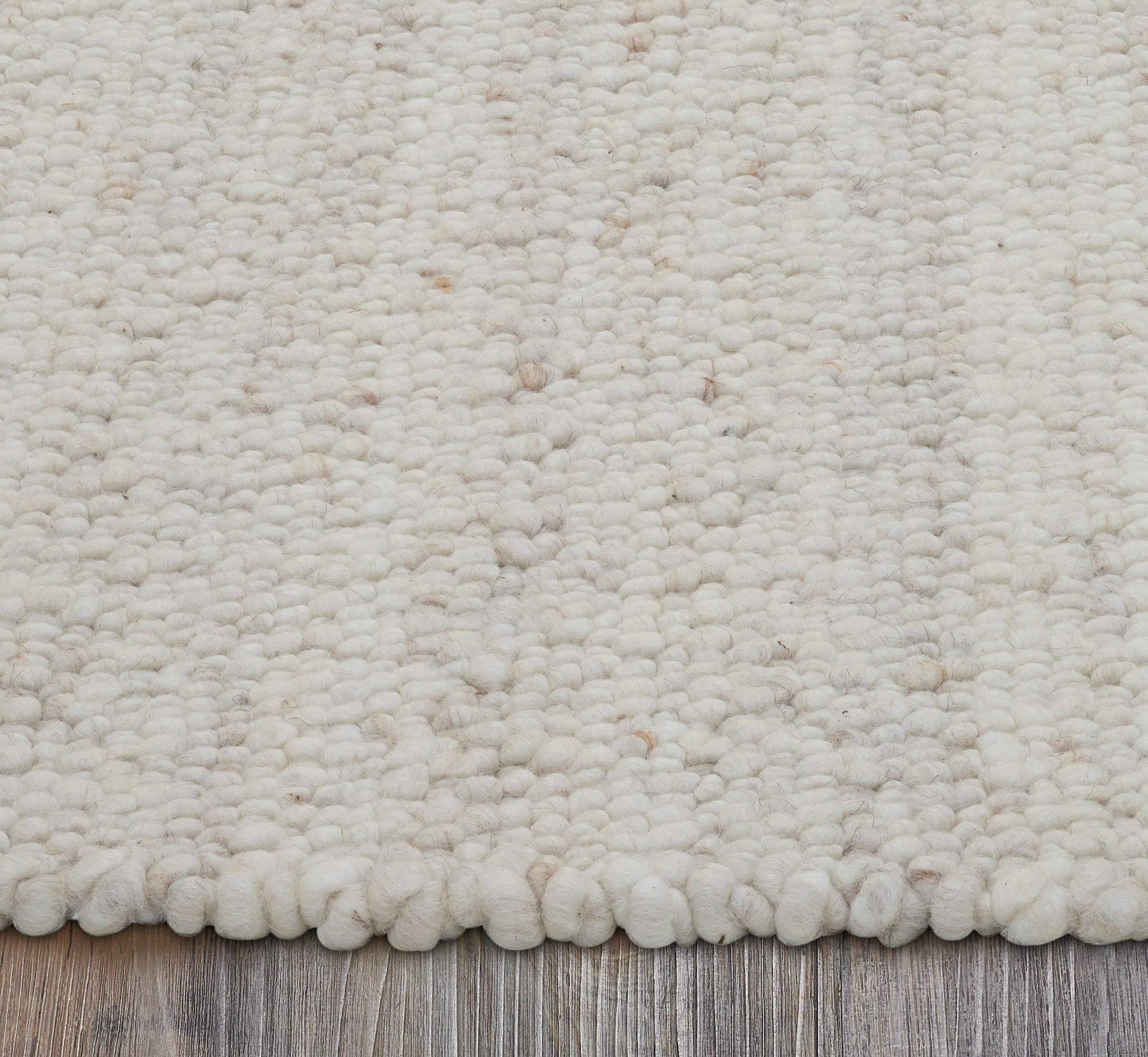 Edge view of Meghan rug showing soft, fluffy texture in cream color on a wooden floor.