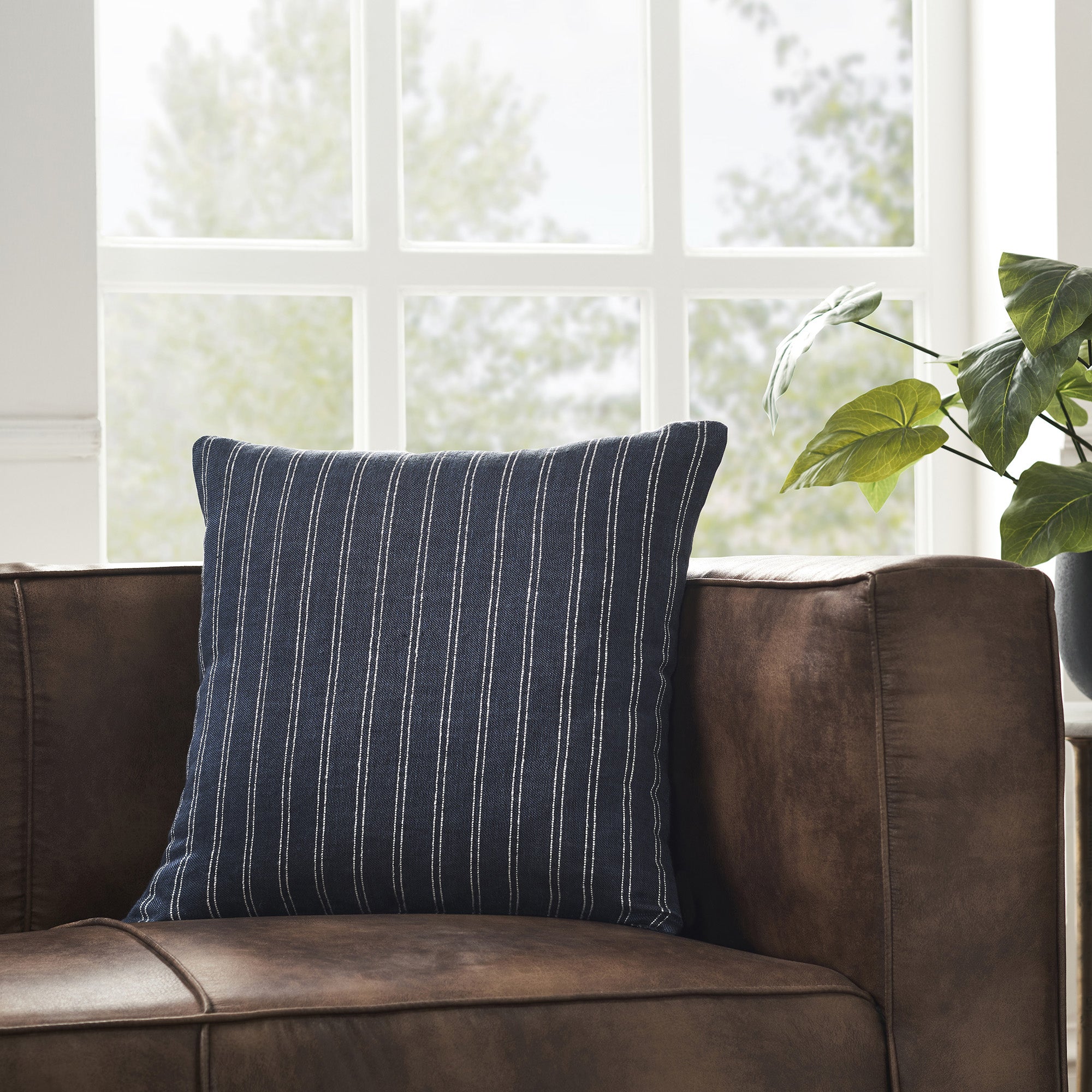 Oakley Indoor Pillow on a brown leather couch, featuring dark blue and white stripes.