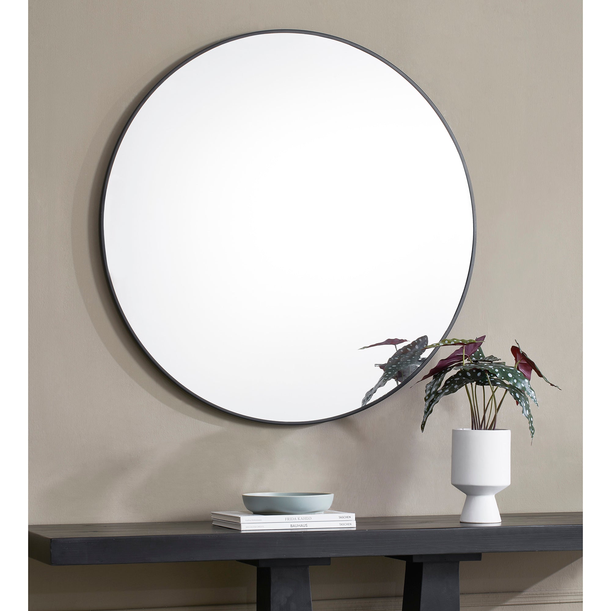 Posadas Wall Mirror with a round shape and black frame, displayed above a console table with decor.