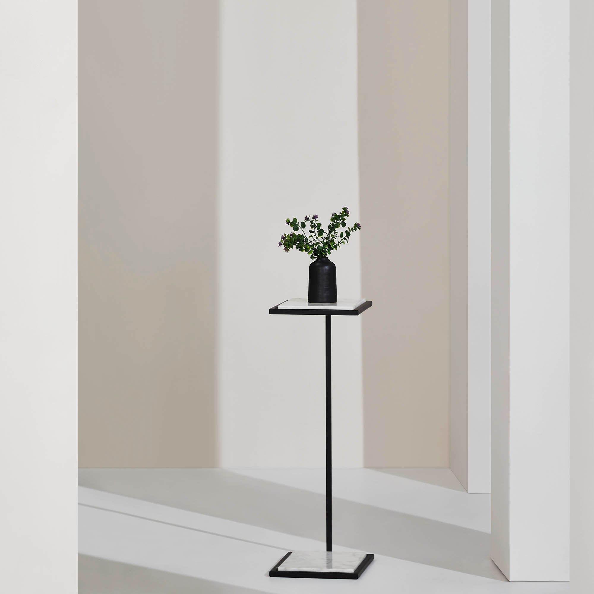 Danica Table by Renwil styled with a black vase and greenery, set against a minimalist background.