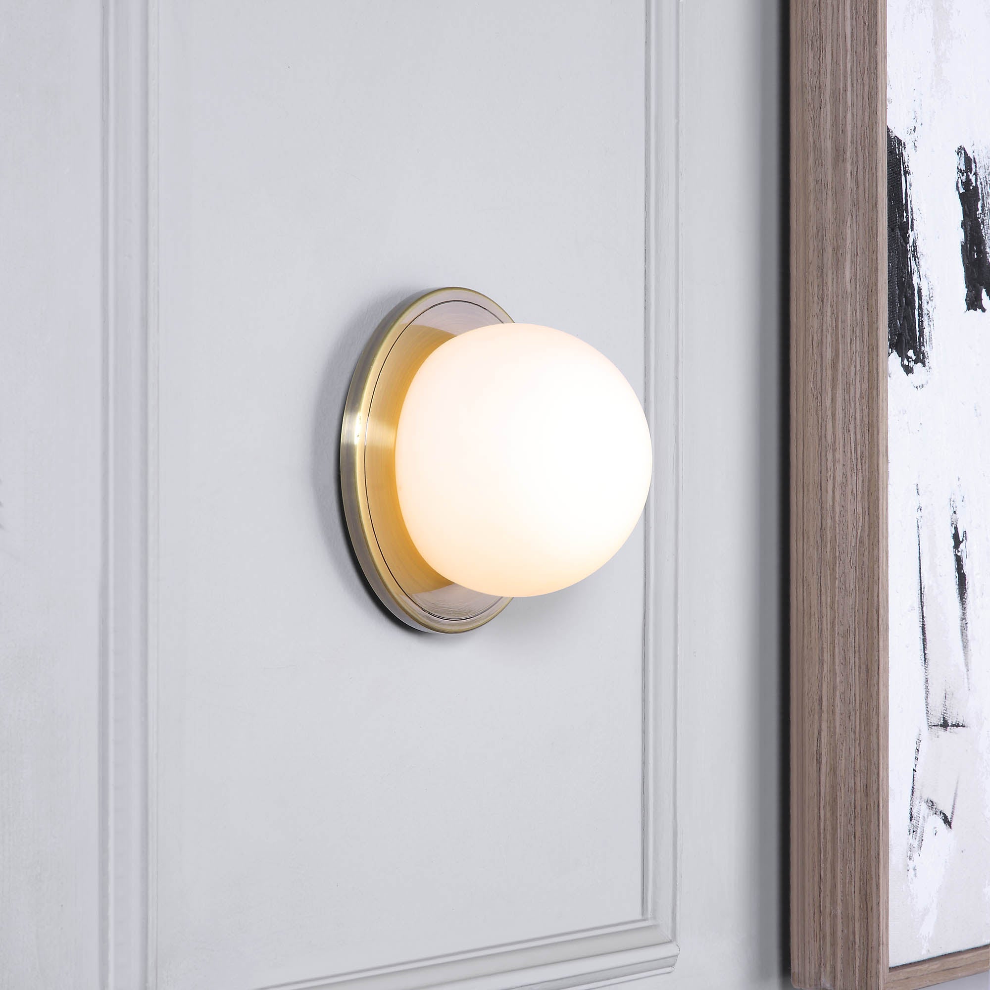 Hugo Wall Sconce mounted on a wall, showcasing its frosted globe and brass details
