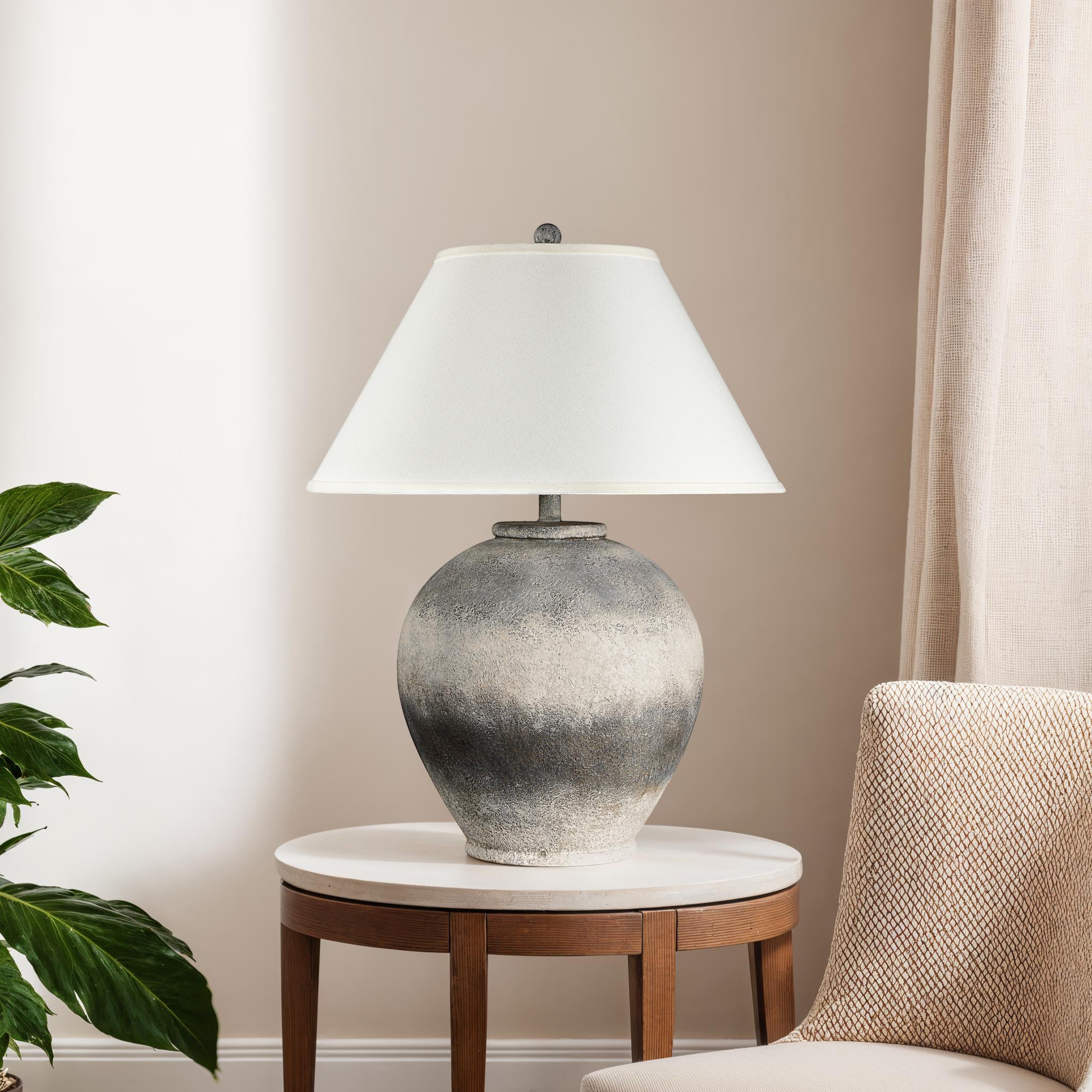 Betulla Table Lamp on a side table in a living room setting, featuring a gray base and white shade.