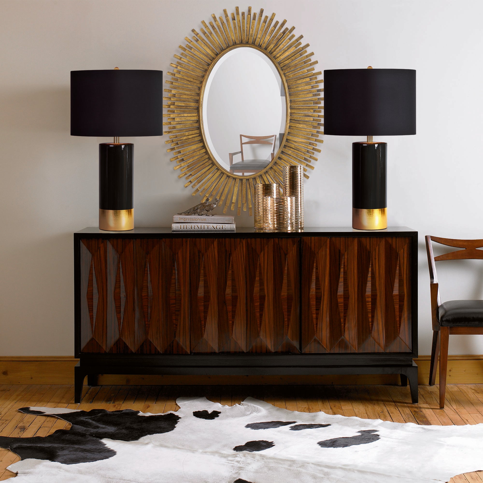 The Tuxedo Table Lamp styled on a sideboard with a sunburst mirror, showcasing its black and gold design.