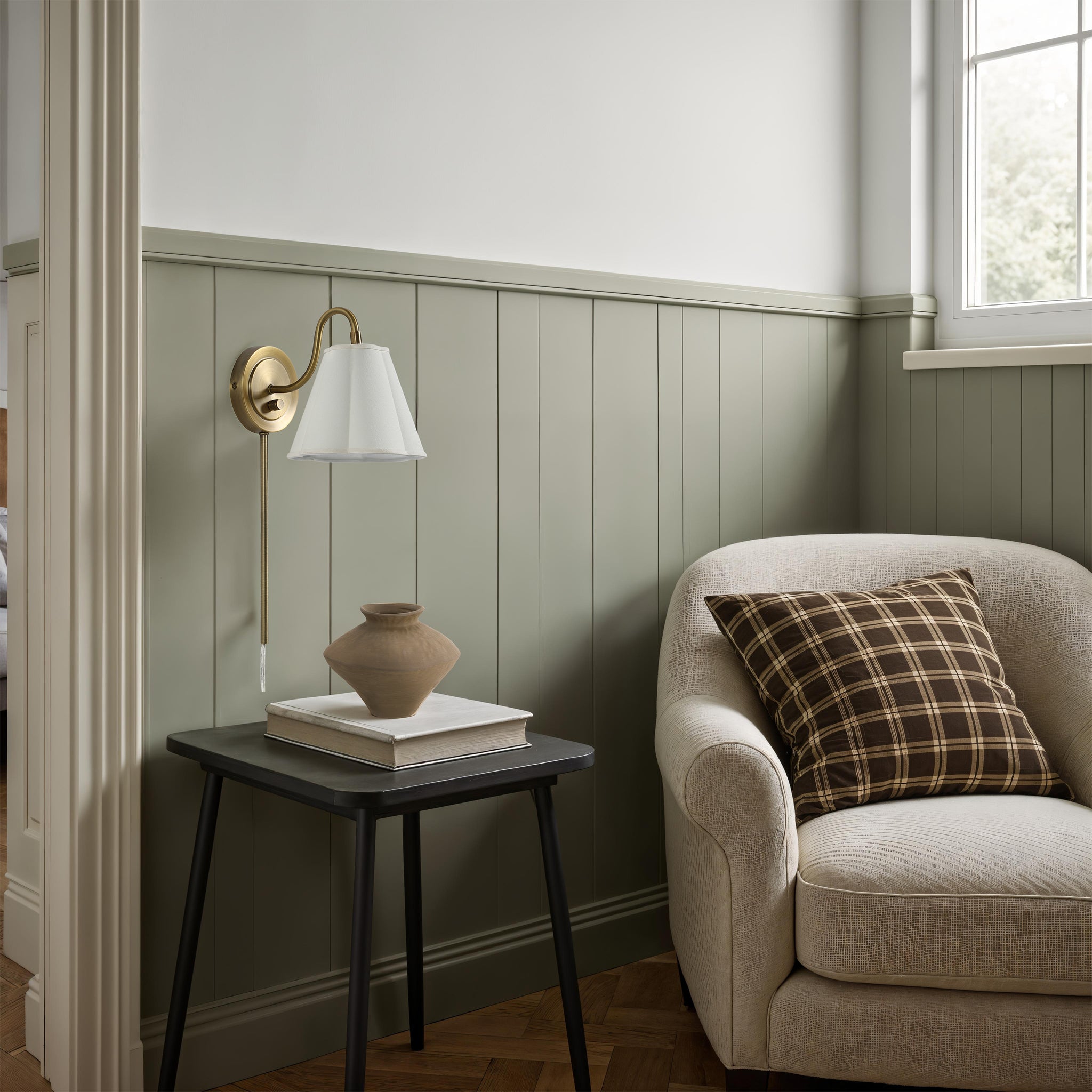 Arielle wall sconce beside a cozy chair, accenting a green paneled wall and decorative vase.