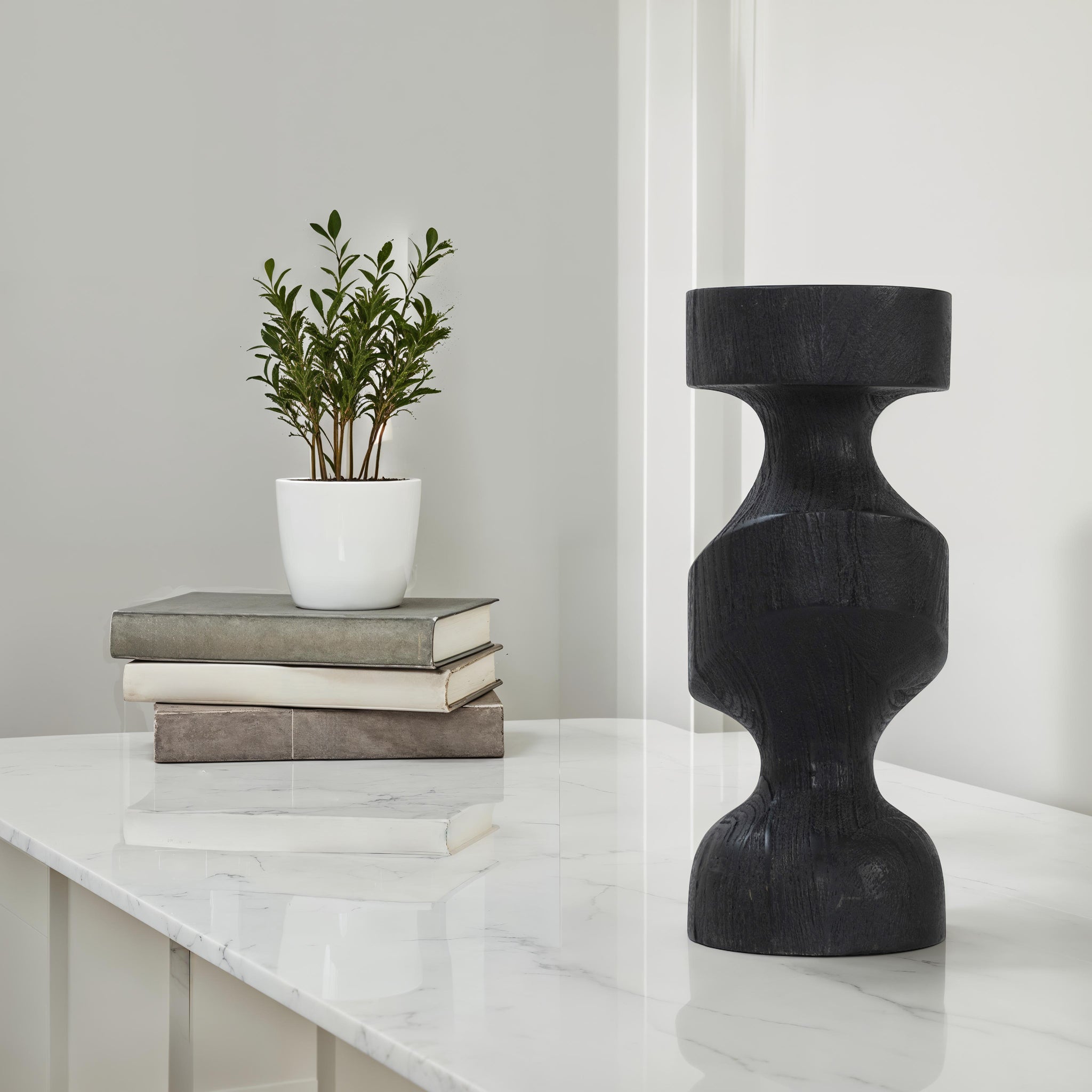 Severn by Renwil black wooden candle holder displayed on a marble table with books and a plant.