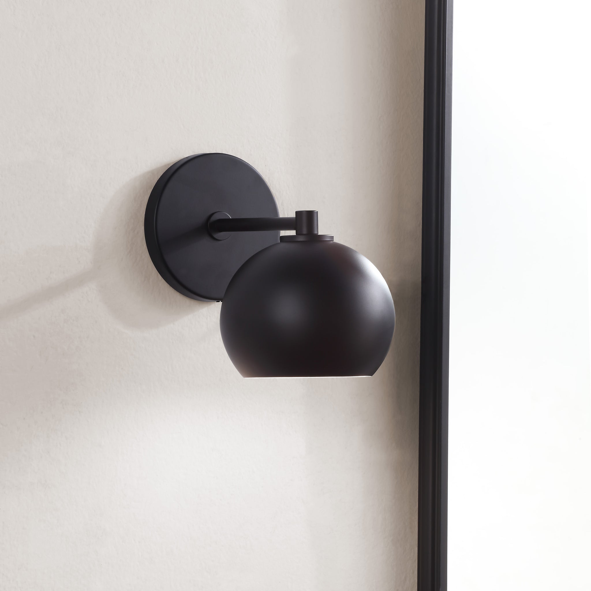 Atia Wall Sconce mounted on a wall, showcasing its round black shade