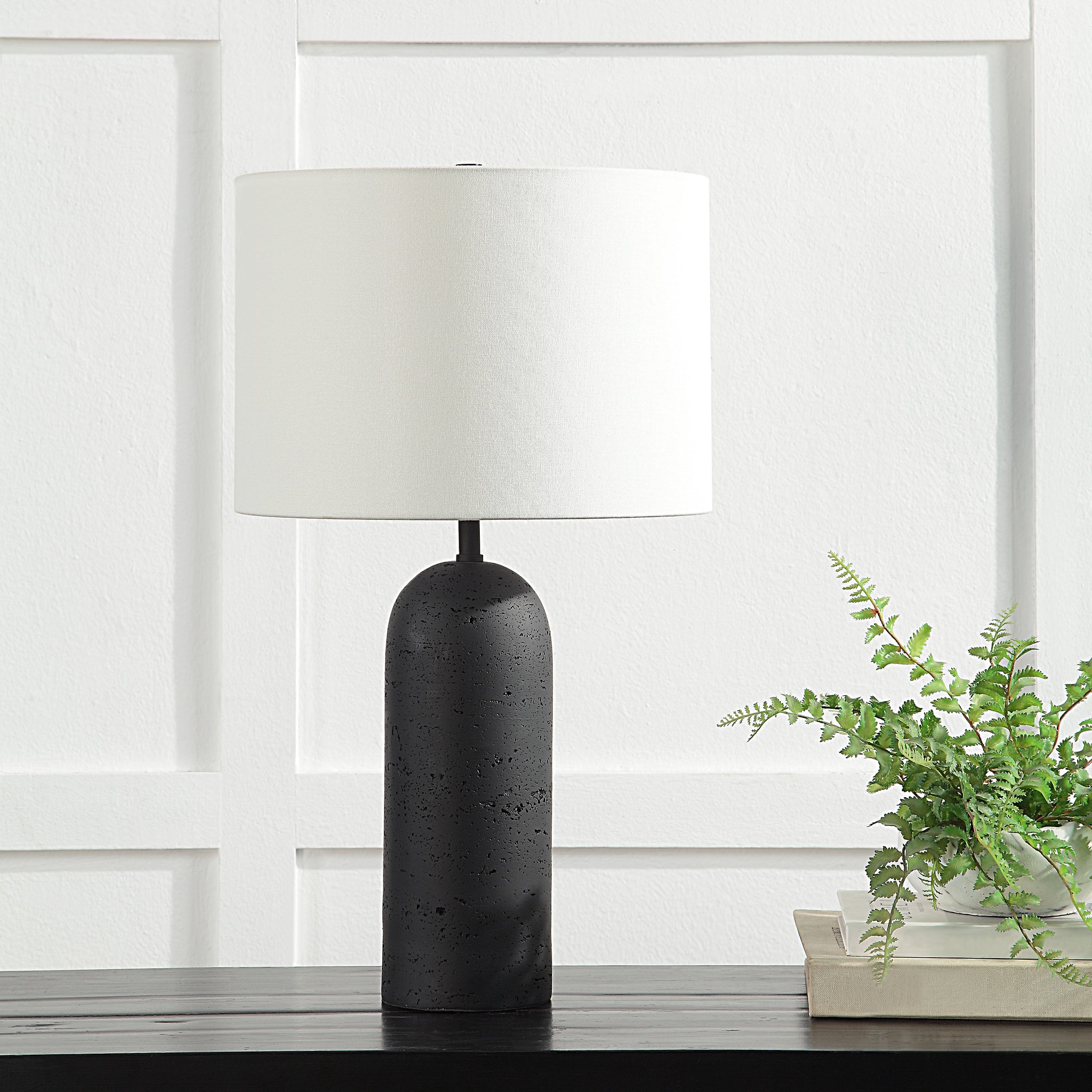 Augusta Table Lamp on a table with a white shade and black base, beside a plant
