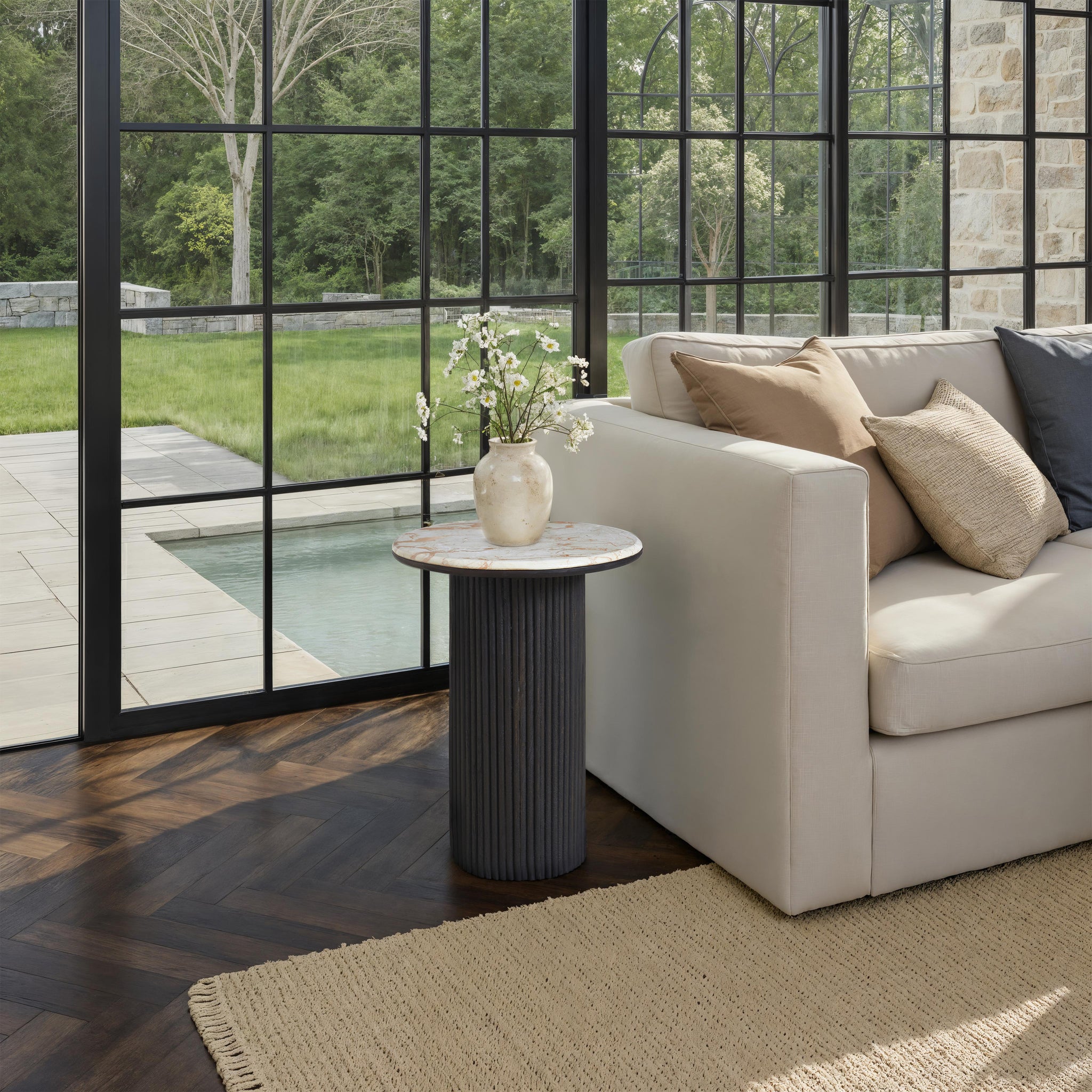 Alessio accent table beside a beige sofa in a bright room with large windows.