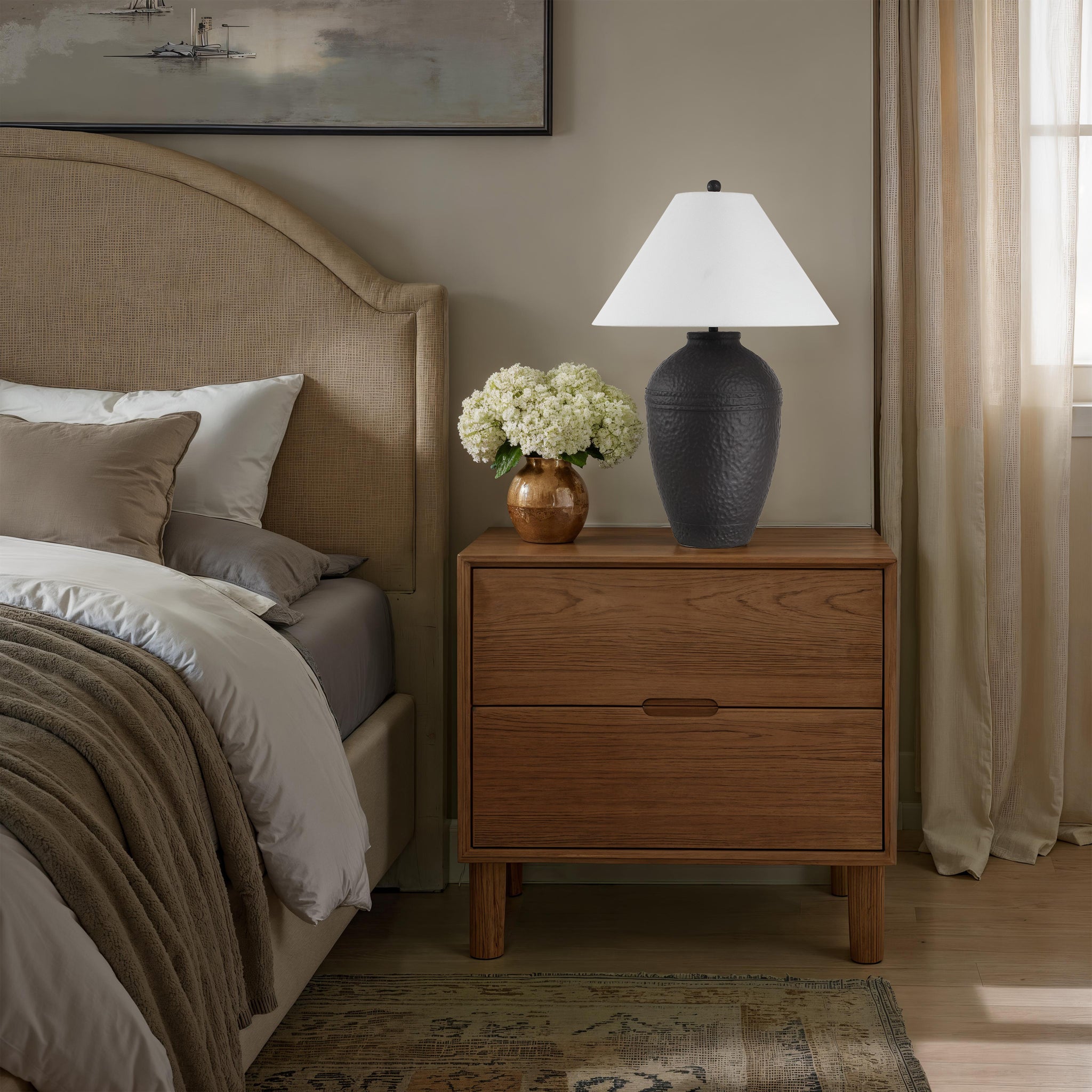 Cupper table lamp by Renwil on a nightstand with flowers, white shade and textured black base.
