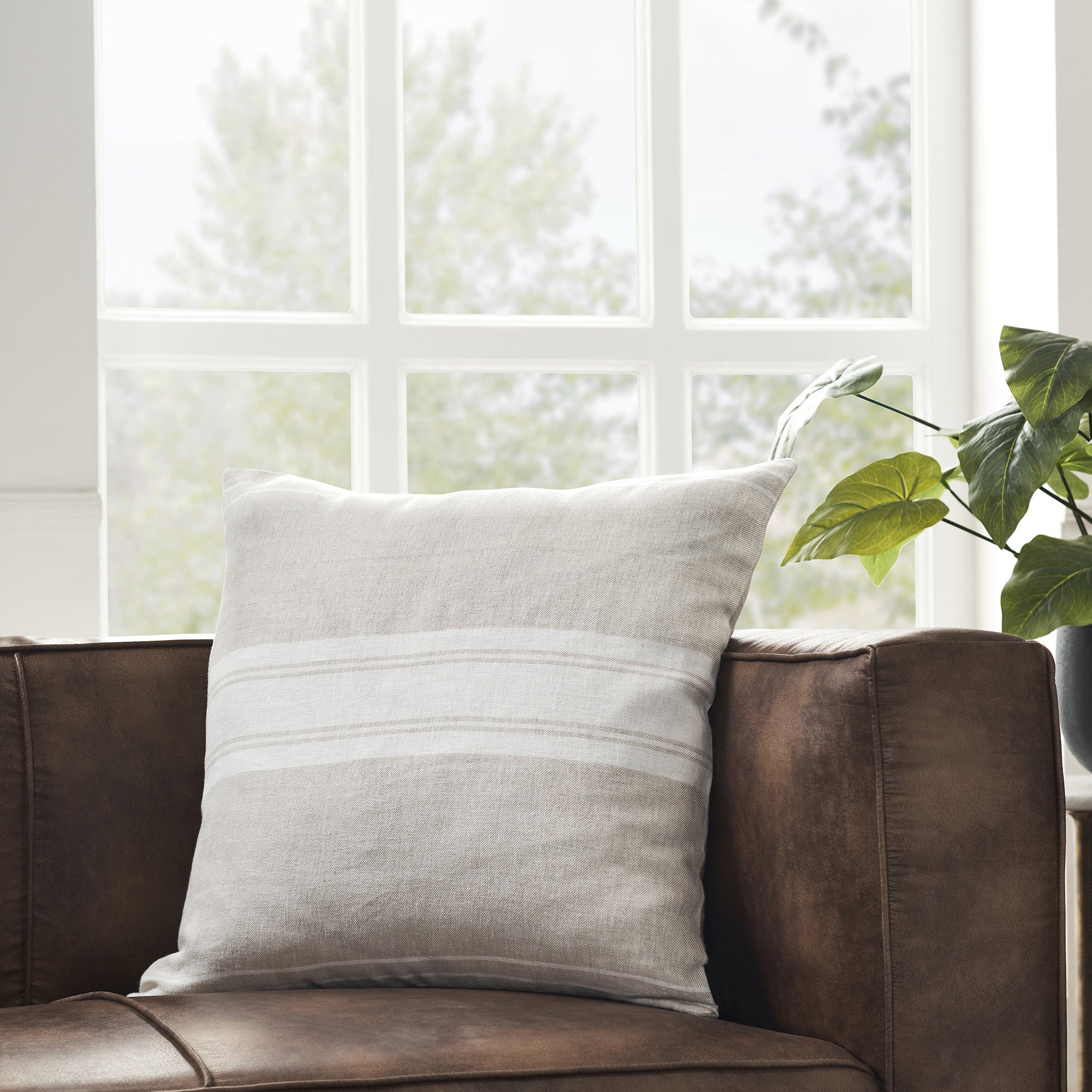 Raelyn Indoor Pillow on a brown leather couch, featuring light gray and white striped design.