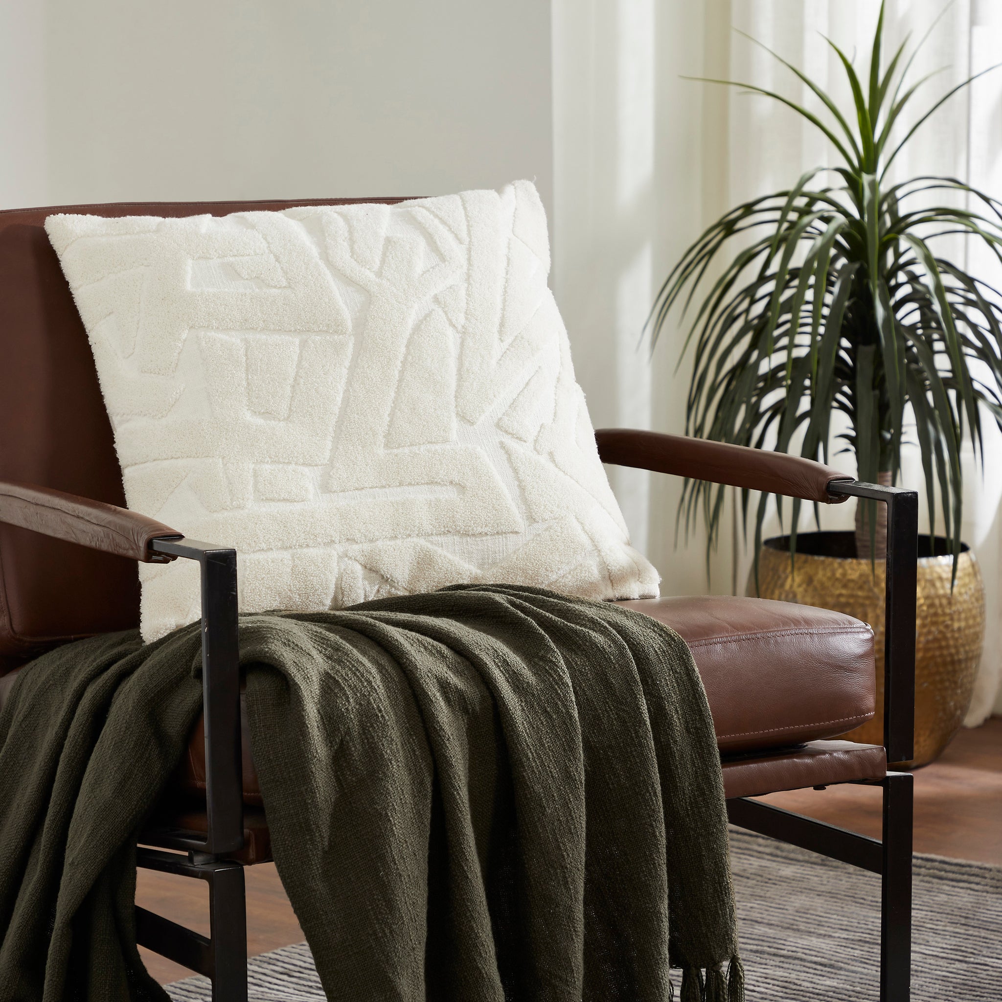 Merano indoor pillow in white displayed on a brown chair with a green throw
