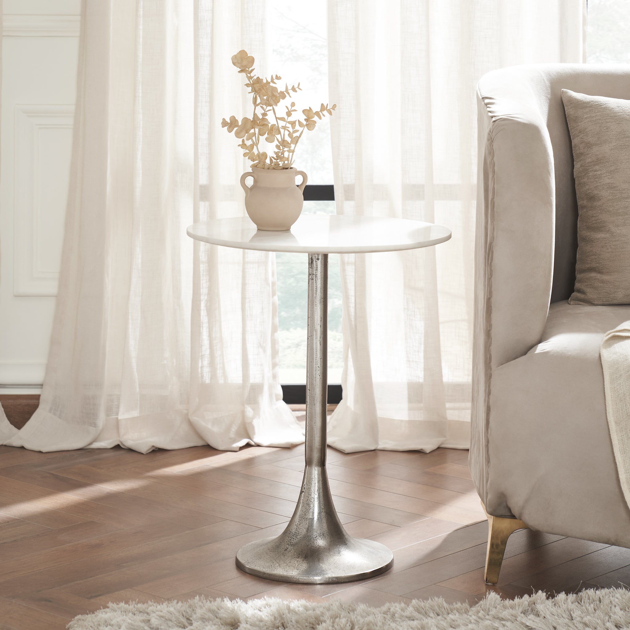 Eloa table beside a sofa, featuring a white marble top and a vase with dried flowers