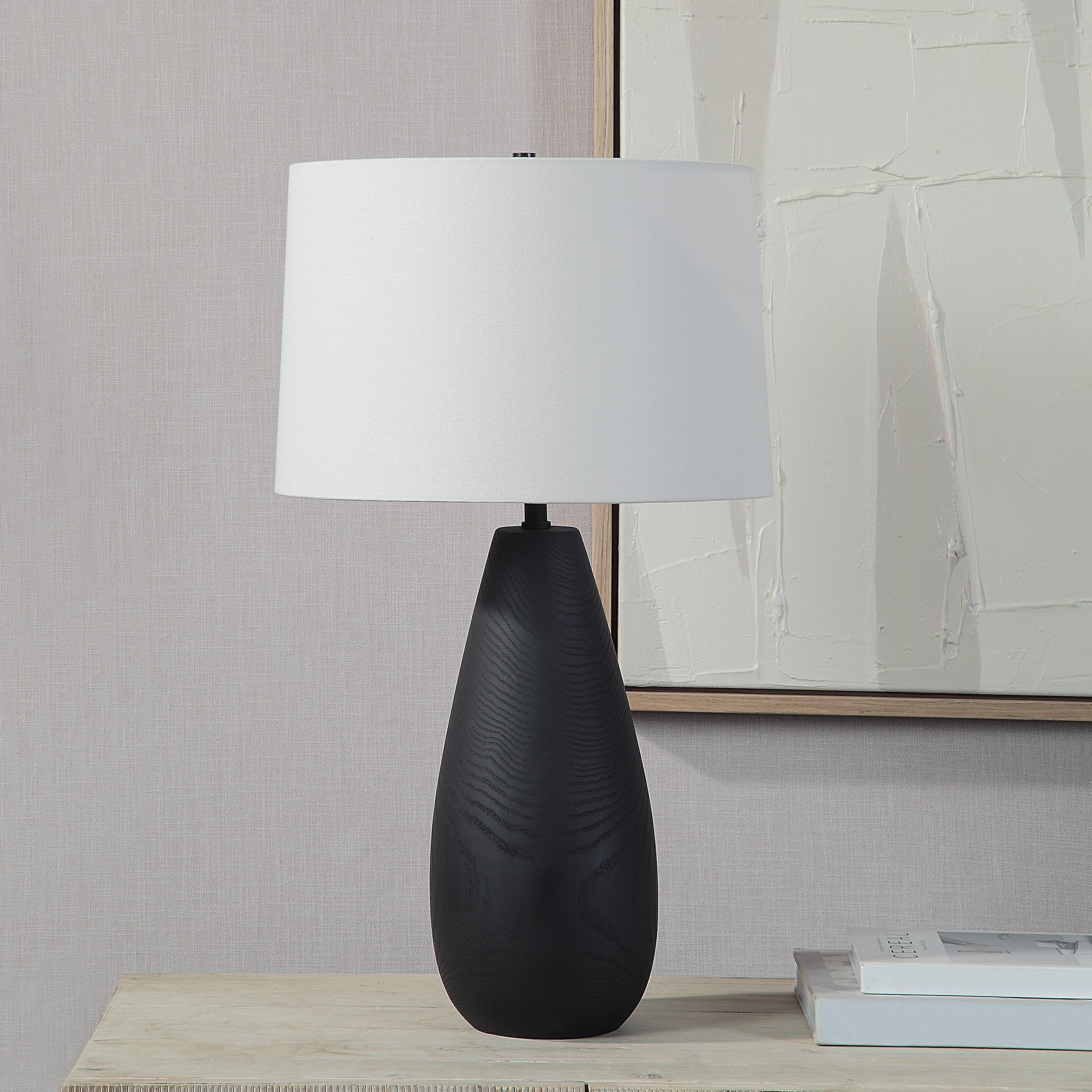 Tala Table Lamp on a table beside a modern artwork, featuring a black base and white shade