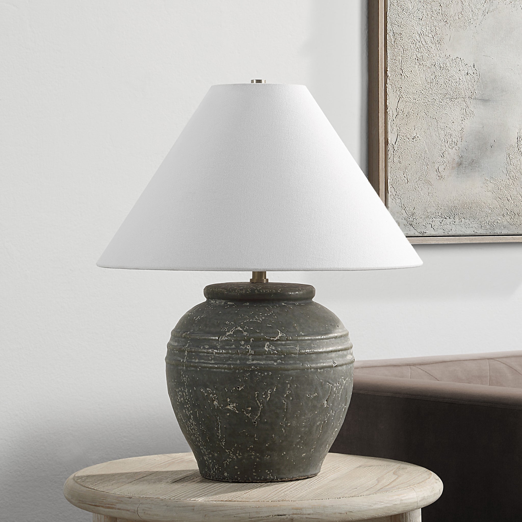 Lino Table Lamp on a wooden table, featuring gray ceramic base and white shade in a living room setting.