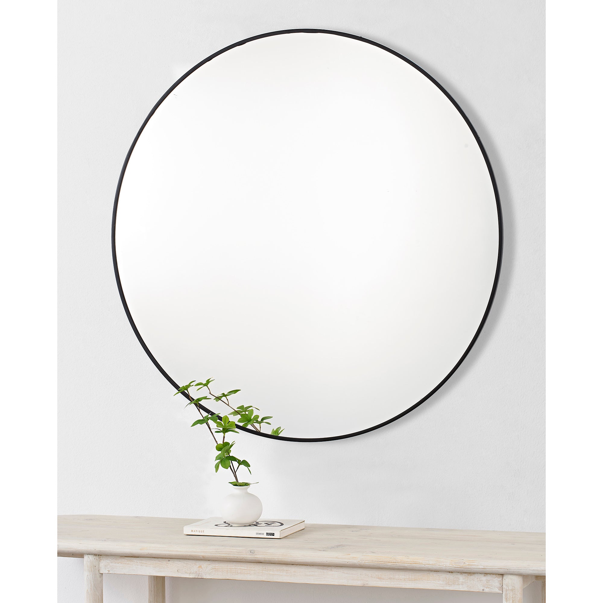 Posadas Wall Mirror, mounted on a wall above a table with a vase and plant, featuring a black frame.