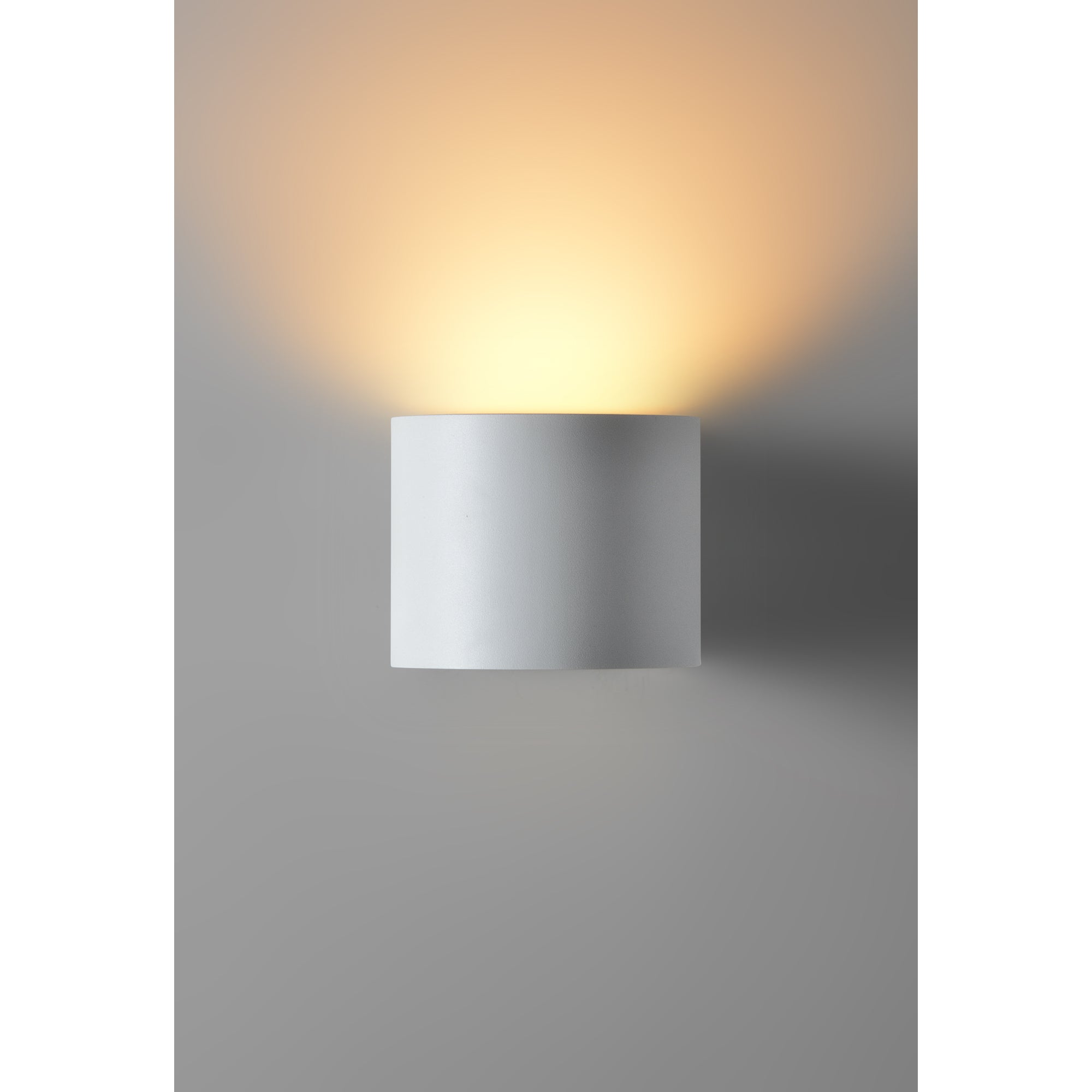 Zak Wall Sconce by Renwil, mounted on gray wall, casting warm light upwards.