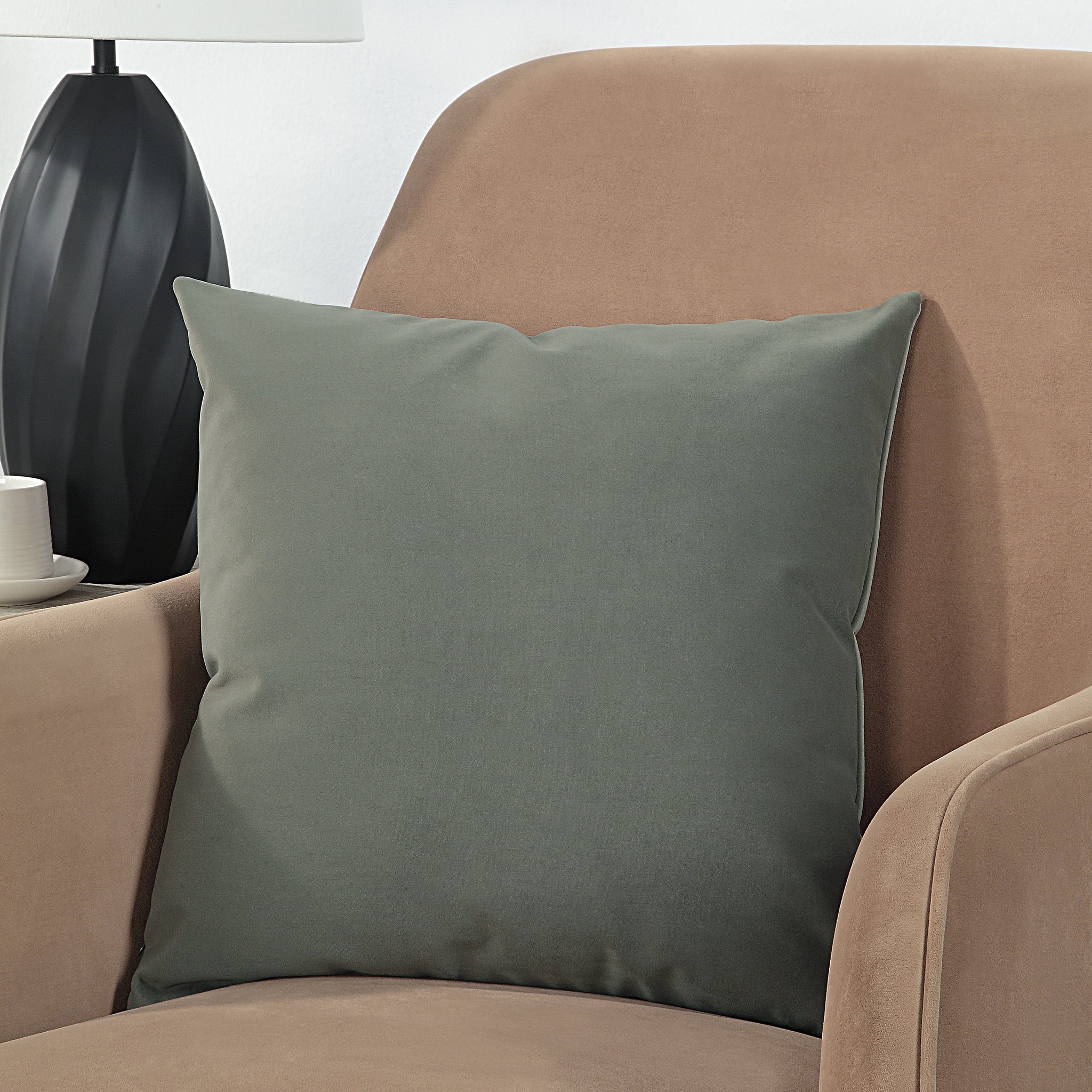 Philemon indoor pillow in dark green, placed on a beige armchair, side view.