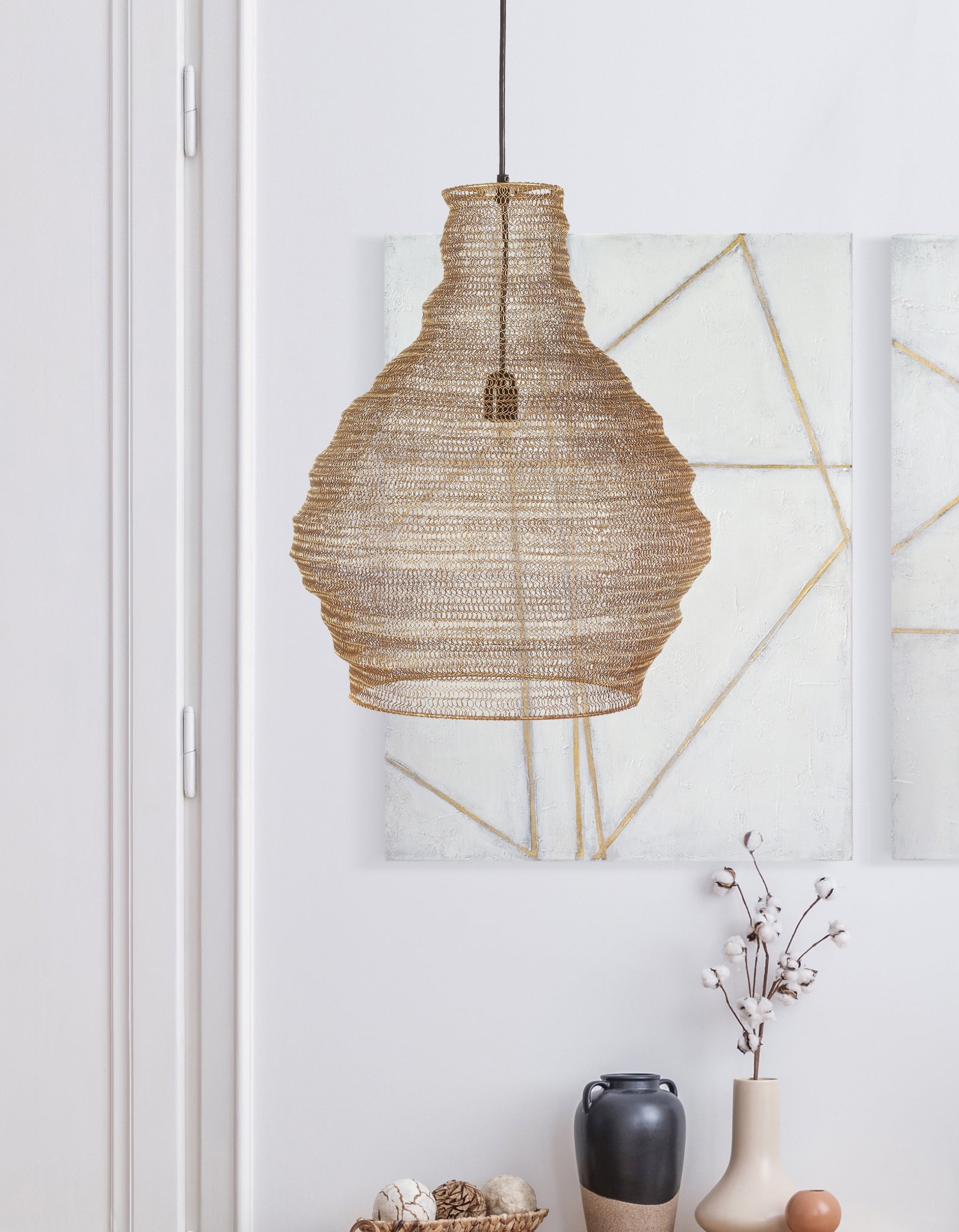 Gere Ceiling Fixture, a woven rattan chandelier in natural tones, hanging against a light wall with abstract art.