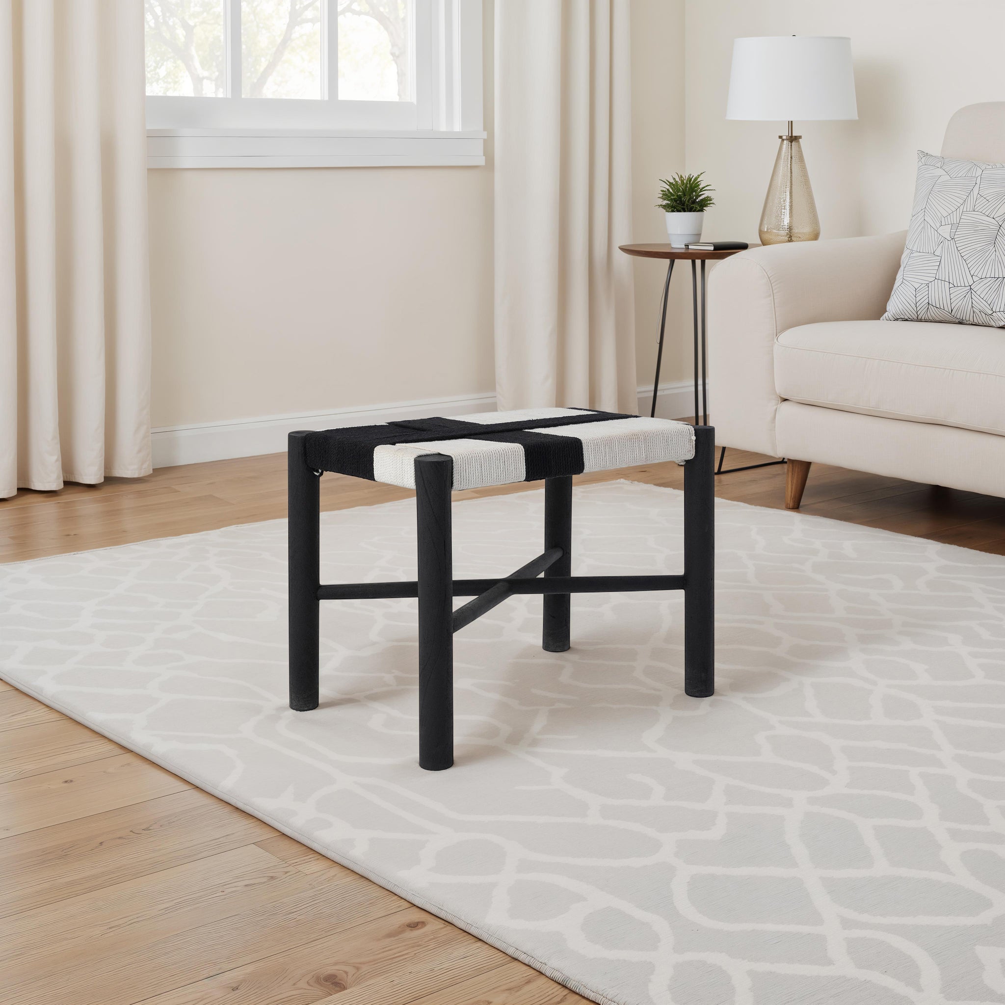 Plex stool by Renwil placed on a patterned rug in a cozy living room with light curtains and a sofa.