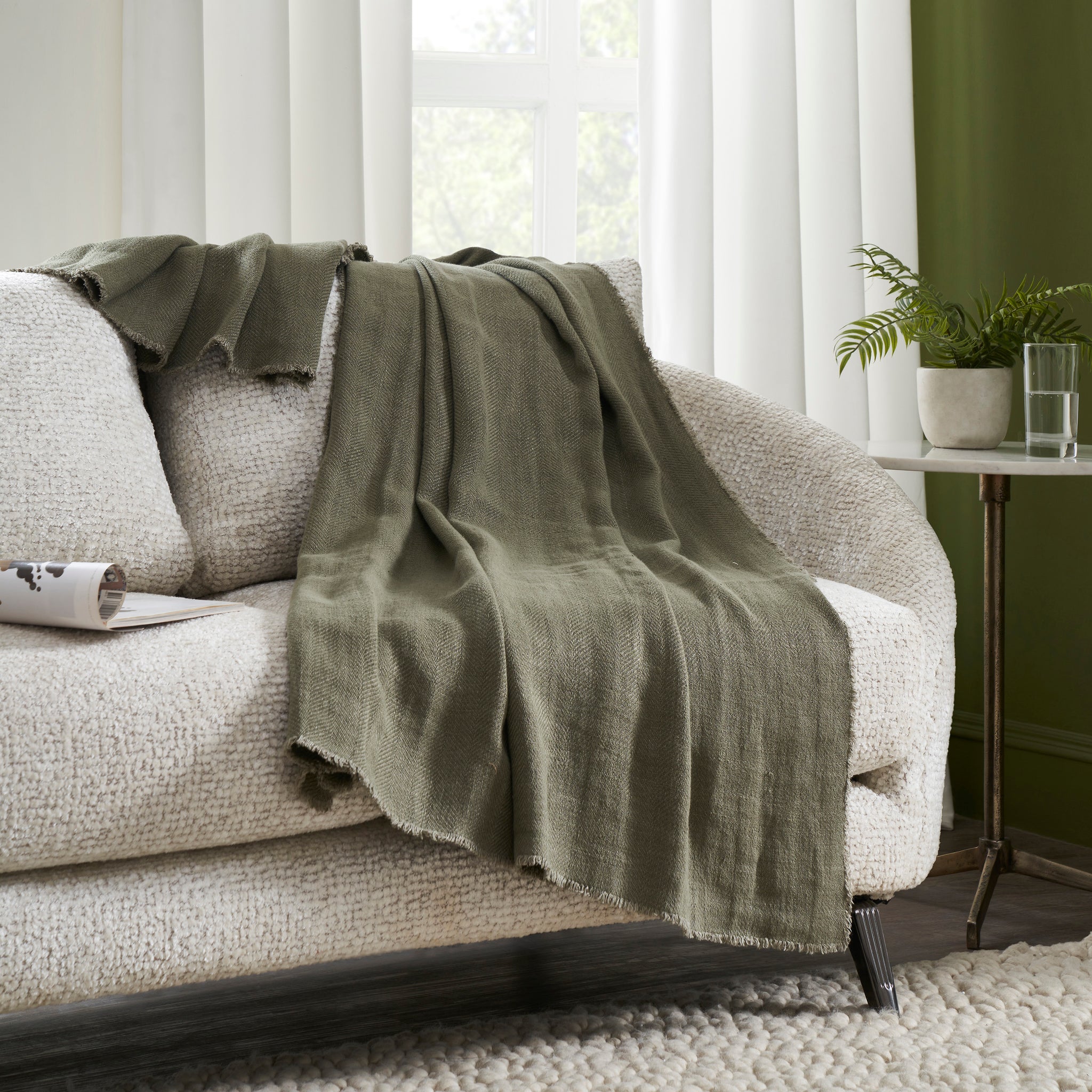 Pisces indoor pillow draped over a cozy sofa, olive green fabric against a textured white backdrop.