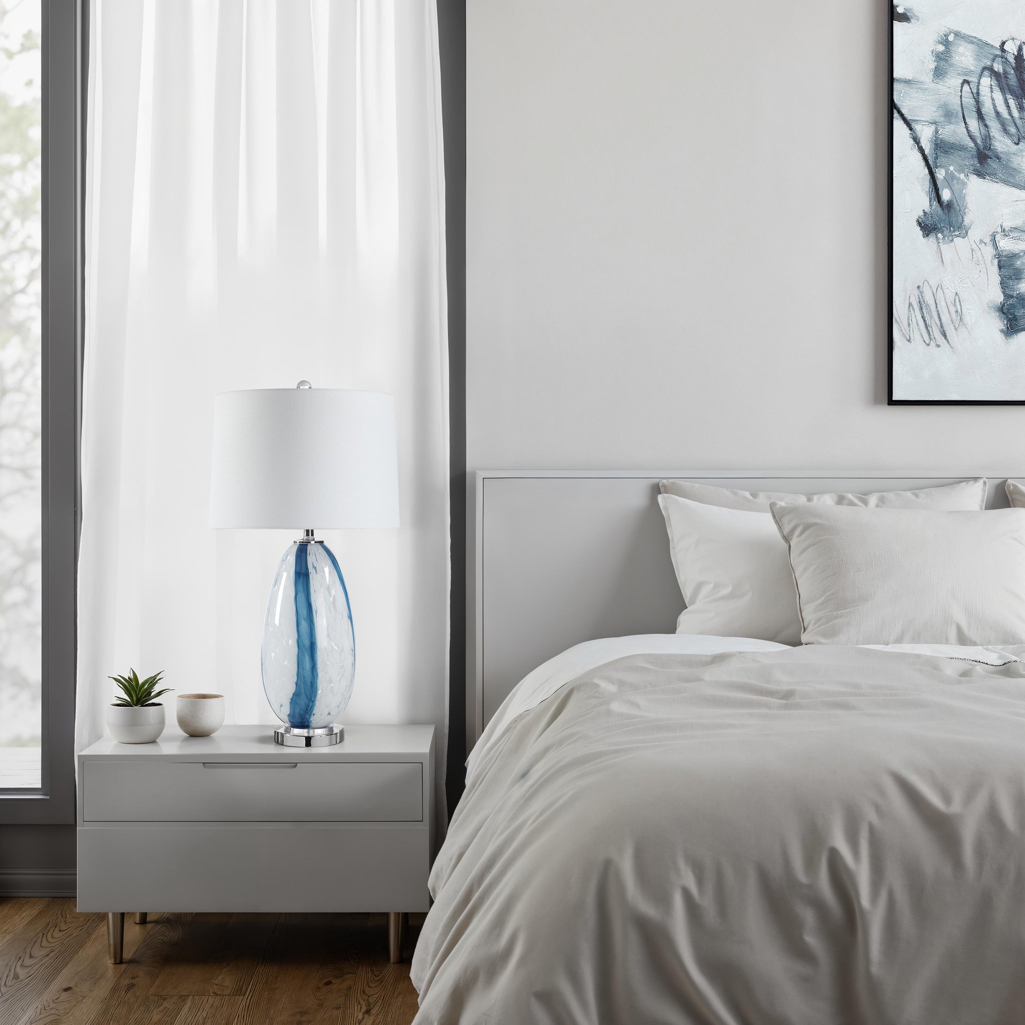 Solis Table Lamp on a nightstand in a modern bedroom, featuring a blue glass base and white shade.