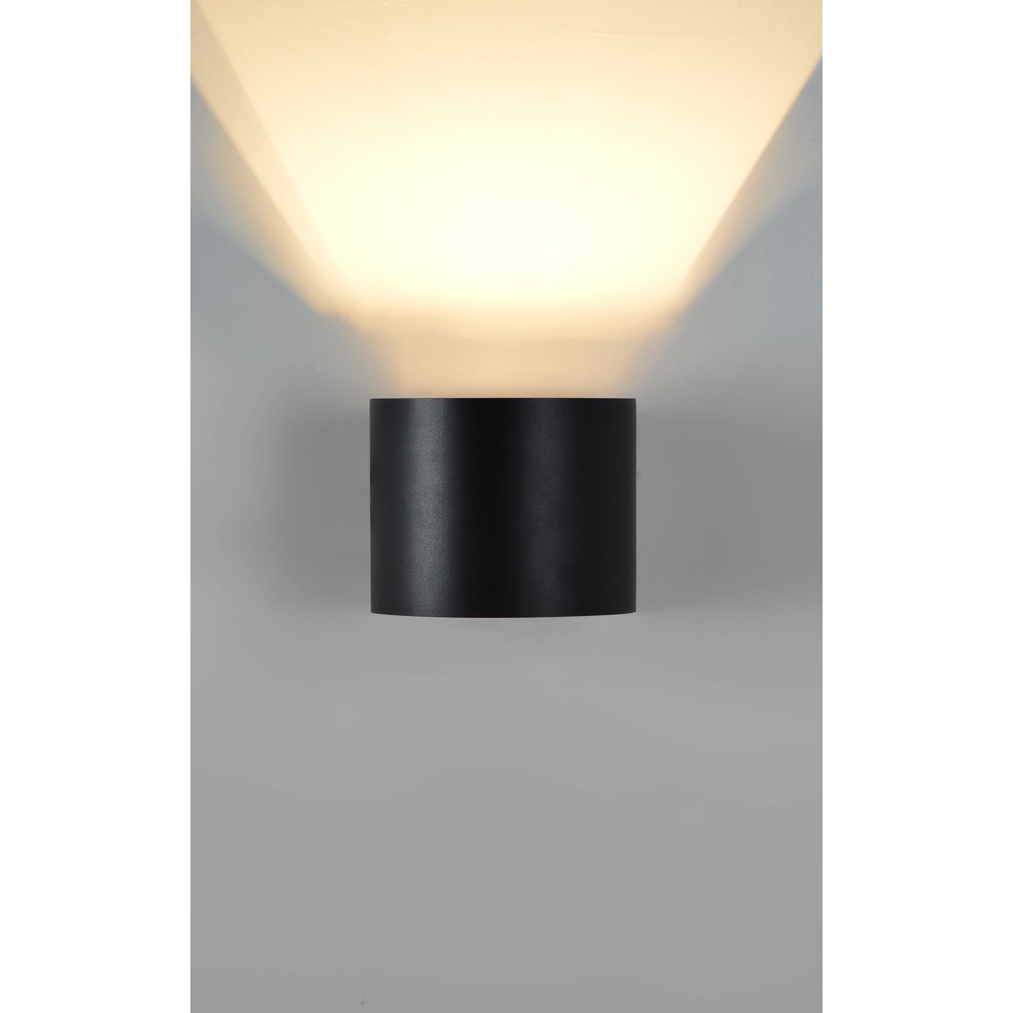 Lark Wall Sconce in matte black mounted on a wall, emitting warm light with a soft glow.