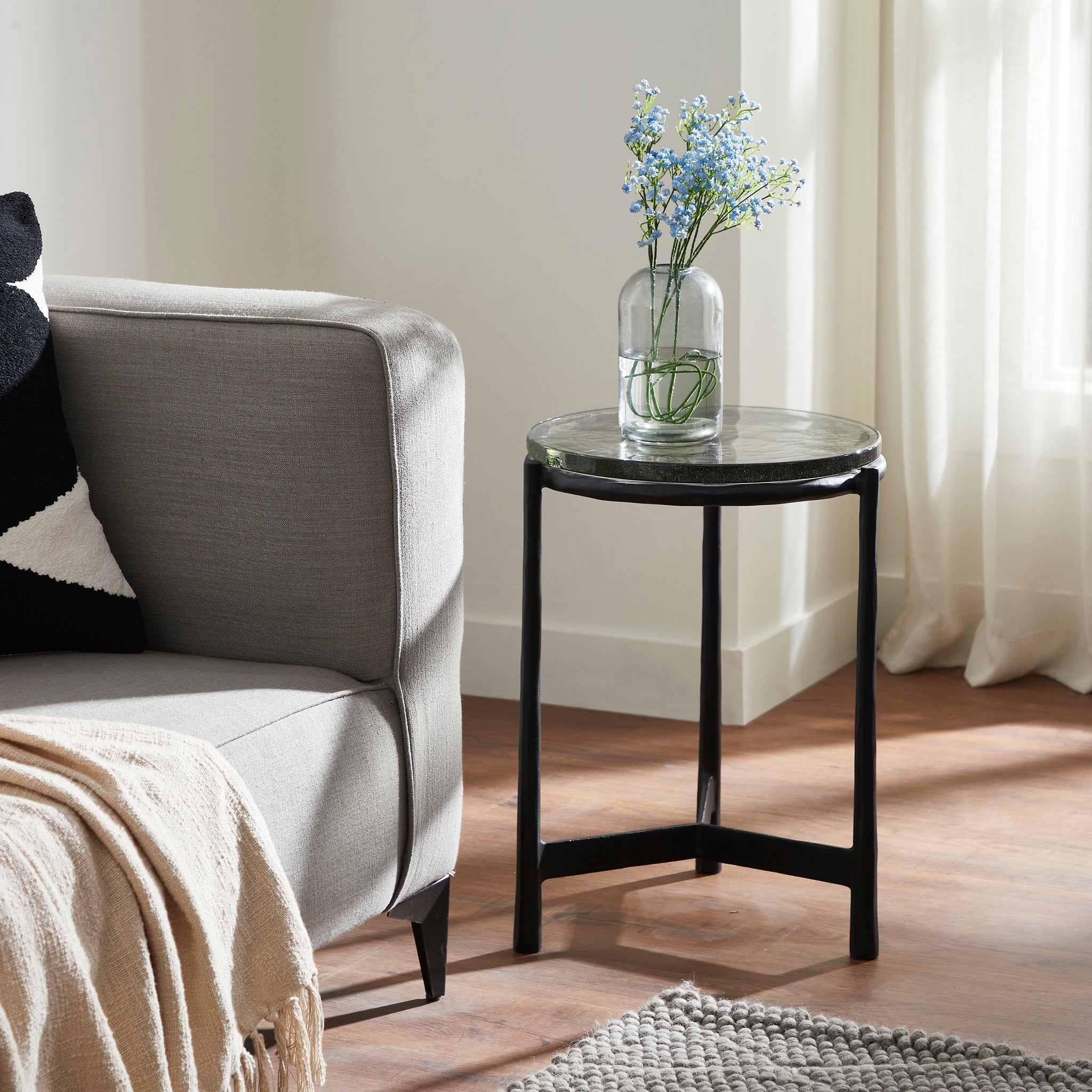 Avila Side Table beside a gray sofa, adorned with a vase of flowers