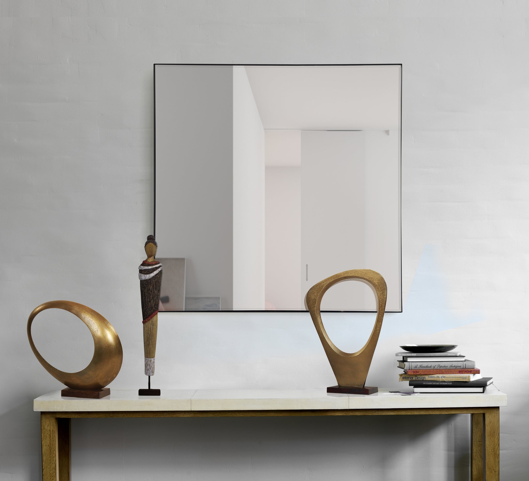 Greer mirror by Renwil displayed above a console table with decorative sculptures and books.