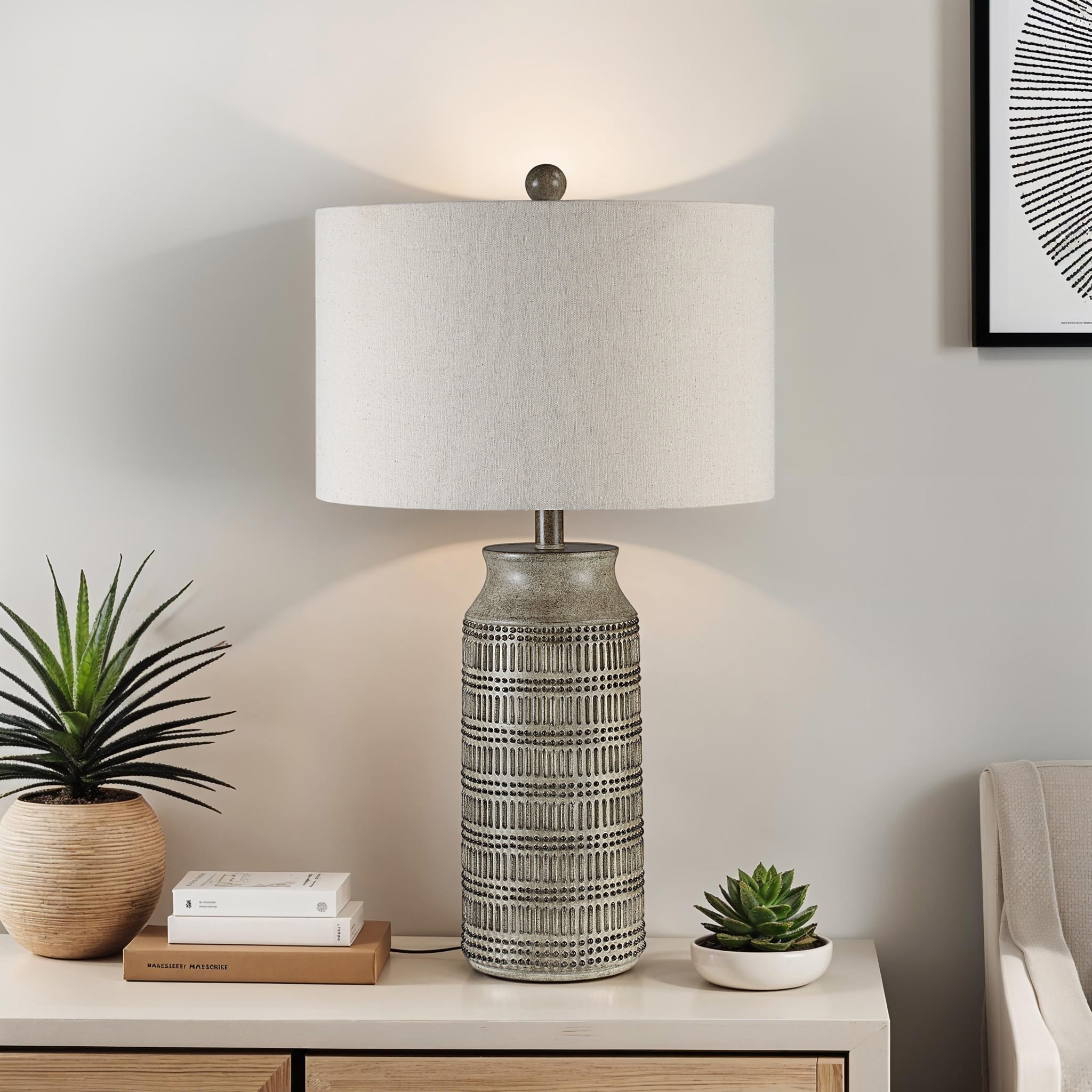 Tarragona Table Lamp on a nightstand with plants and books, showcasing its gray ceramic base and beige shade.