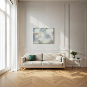 Bellis wall art featuring abstract blue and beige tones in a gold frame, displayed above a light sofa in a bright room.
