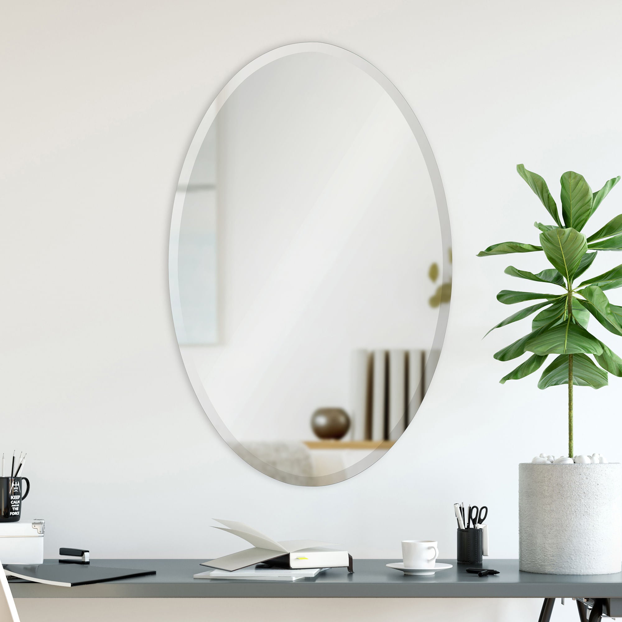 Frances oval mirror with a sleek silver frame, mounted on a light wall above a modern desk with a plant.