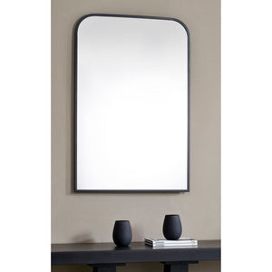 Jackline mirror with a sleek black frame, featuring a rounded top, mounted on a beige wall above a black table with decorative vases.