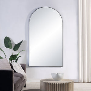 Farida mirror with an arched top, featuring a sleek black frame, displayed against a light wall near a sofa and plant.