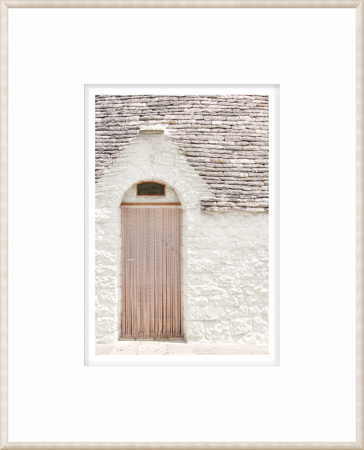 Masonry wall art featuring a white stone wall with a wooden door and hanging strands in Alberobello, Italy.