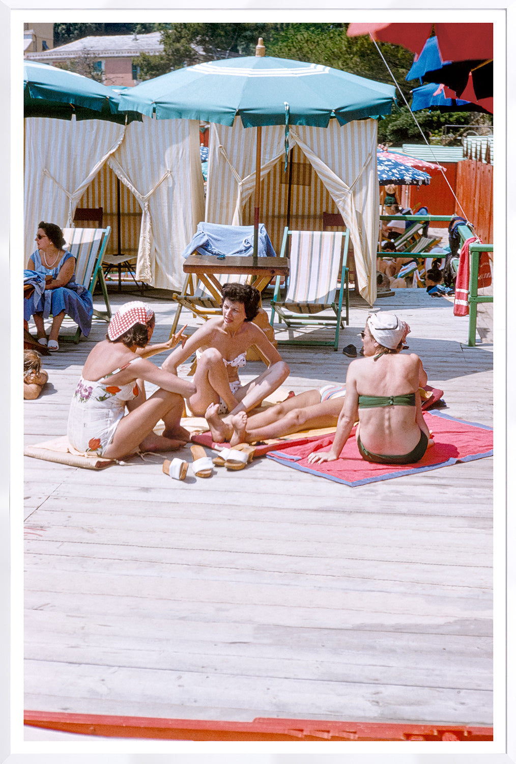 Toni Frissell – Gossip Riviera C. 1954, women relaxing on a beach with umbrellas and lounge chairs.