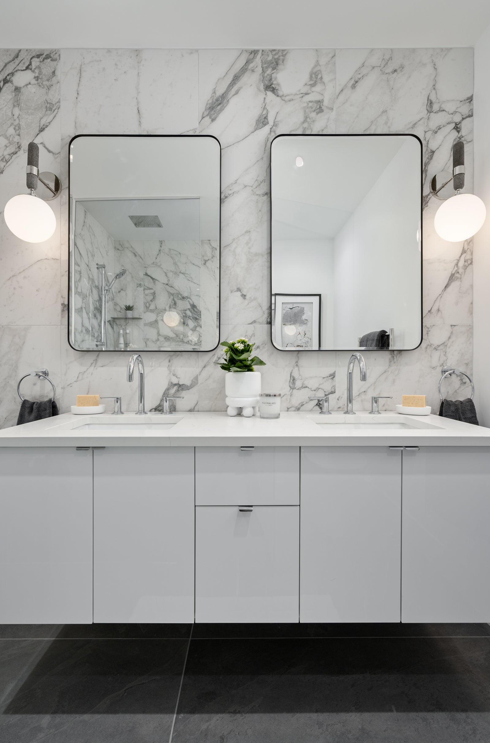 Marble double-vanity bathroom framed by black-rimmed mirrors and globe wall sconces.