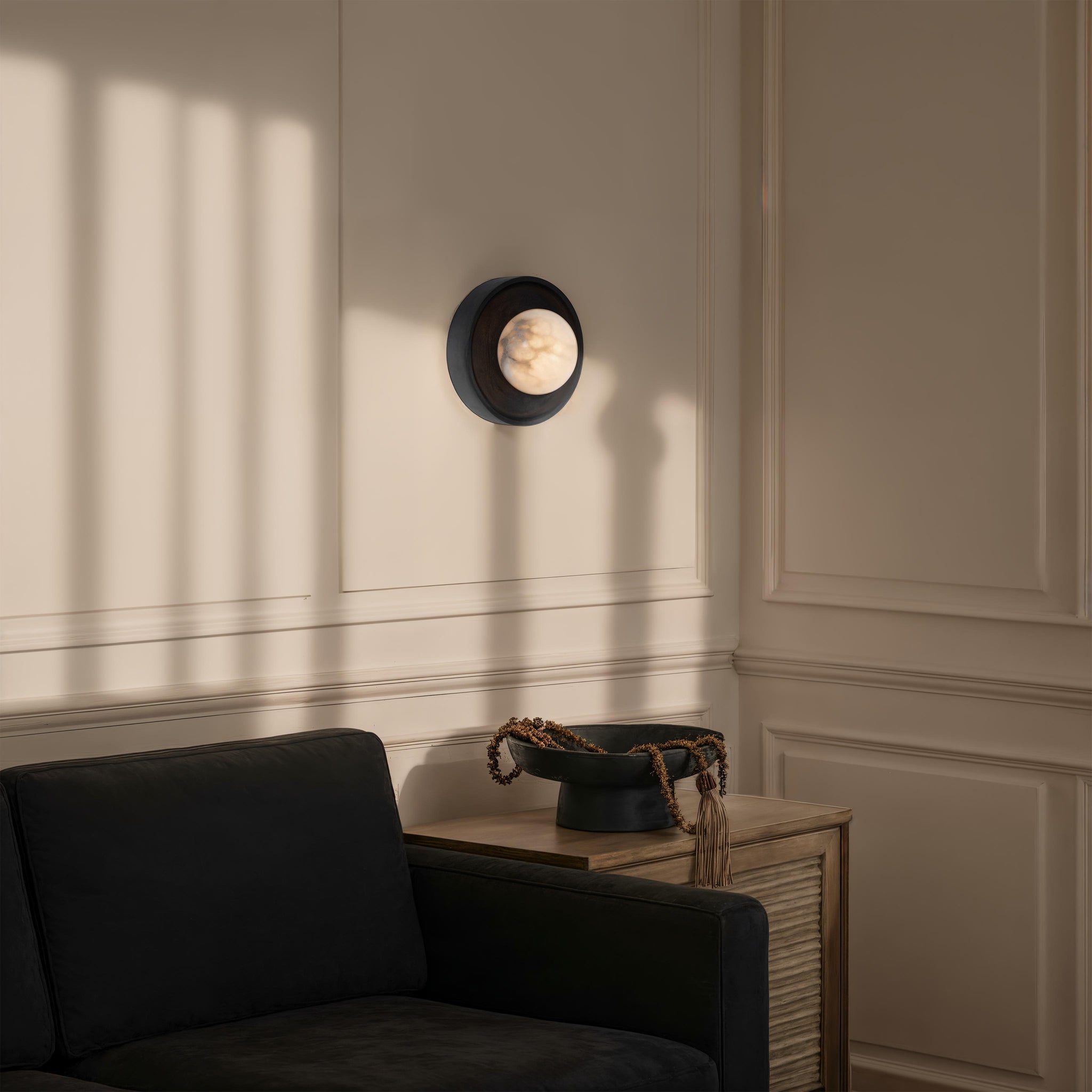 Haloa wall sconce positioned on a light wall, casting shadows near a black sofa