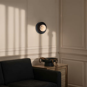 Haloa wall sconce positioned on a light wall, casting shadows near a black sofa