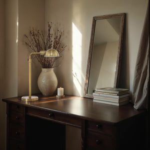 Halle Table Lamp on a wooden desk, surrounded by books, a vase, and a candle in a cozy setting.