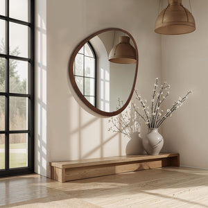 Borago mirror with a rounded wooden frame, reflecting a modern interior with a wooden bench and vase of branches.