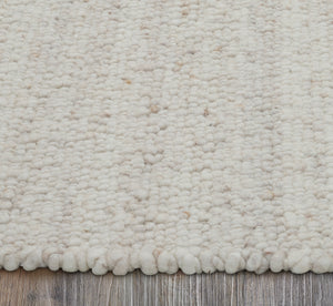 Edge view of Meghan rug showing soft, fluffy texture in cream color on a wooden floor.