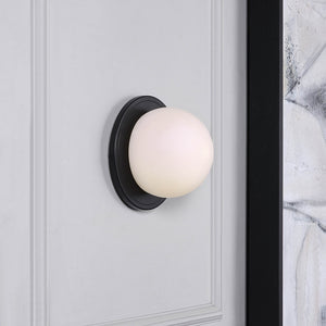 Sybil Wall Sconce installed on a gray wall, showcasing a white glass shade and black base