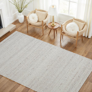 Meghan rug in light beige with textured pattern, placed on wooden floor near two chairs and a lamp.
