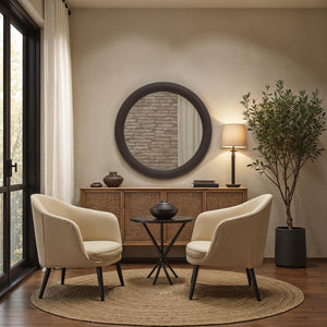 Potro mirror with a round black frame reflecting a cozy room with beige chairs, a wooden table, and a plant.