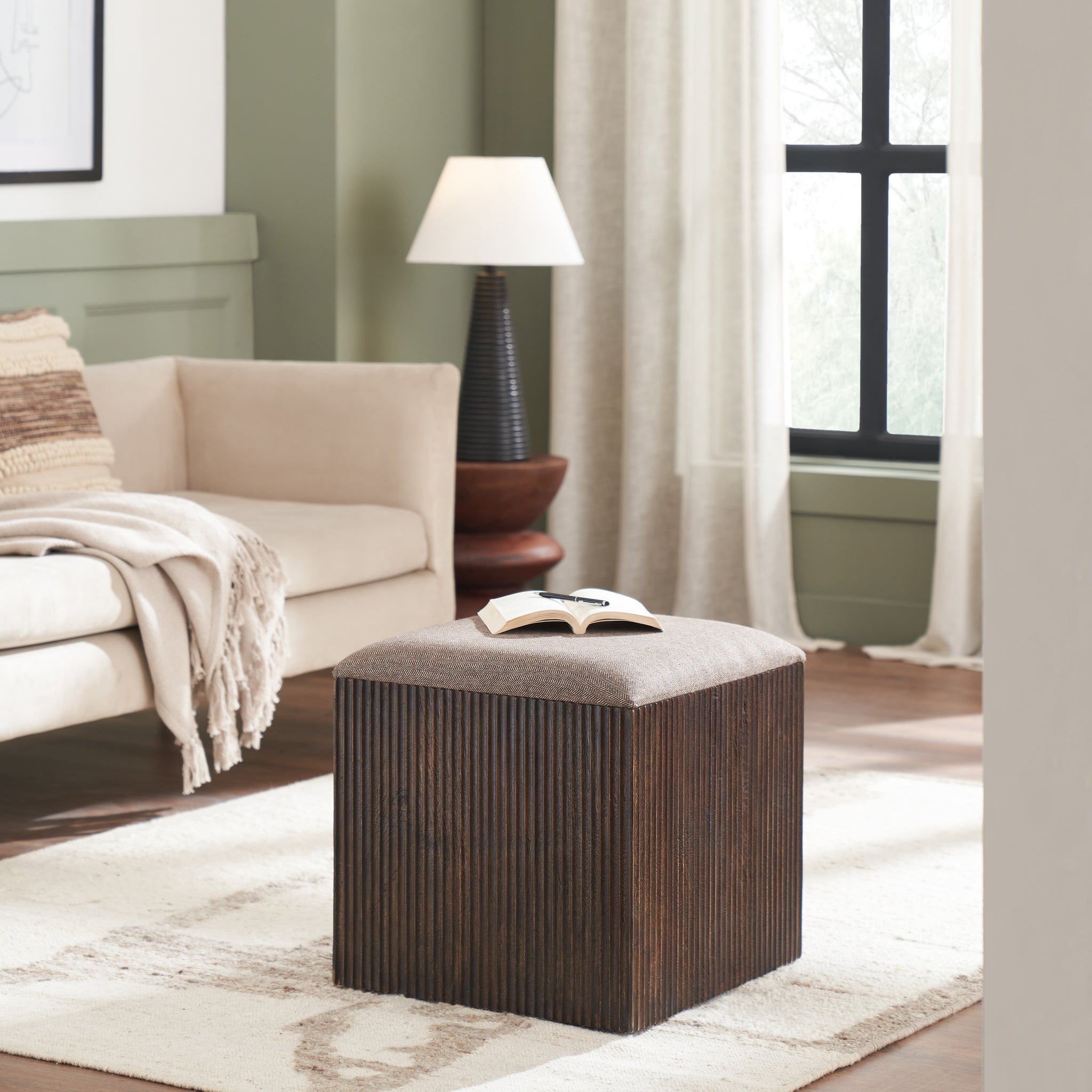 Tristan stool in a living room setting with a book on top, next to a sofa.
